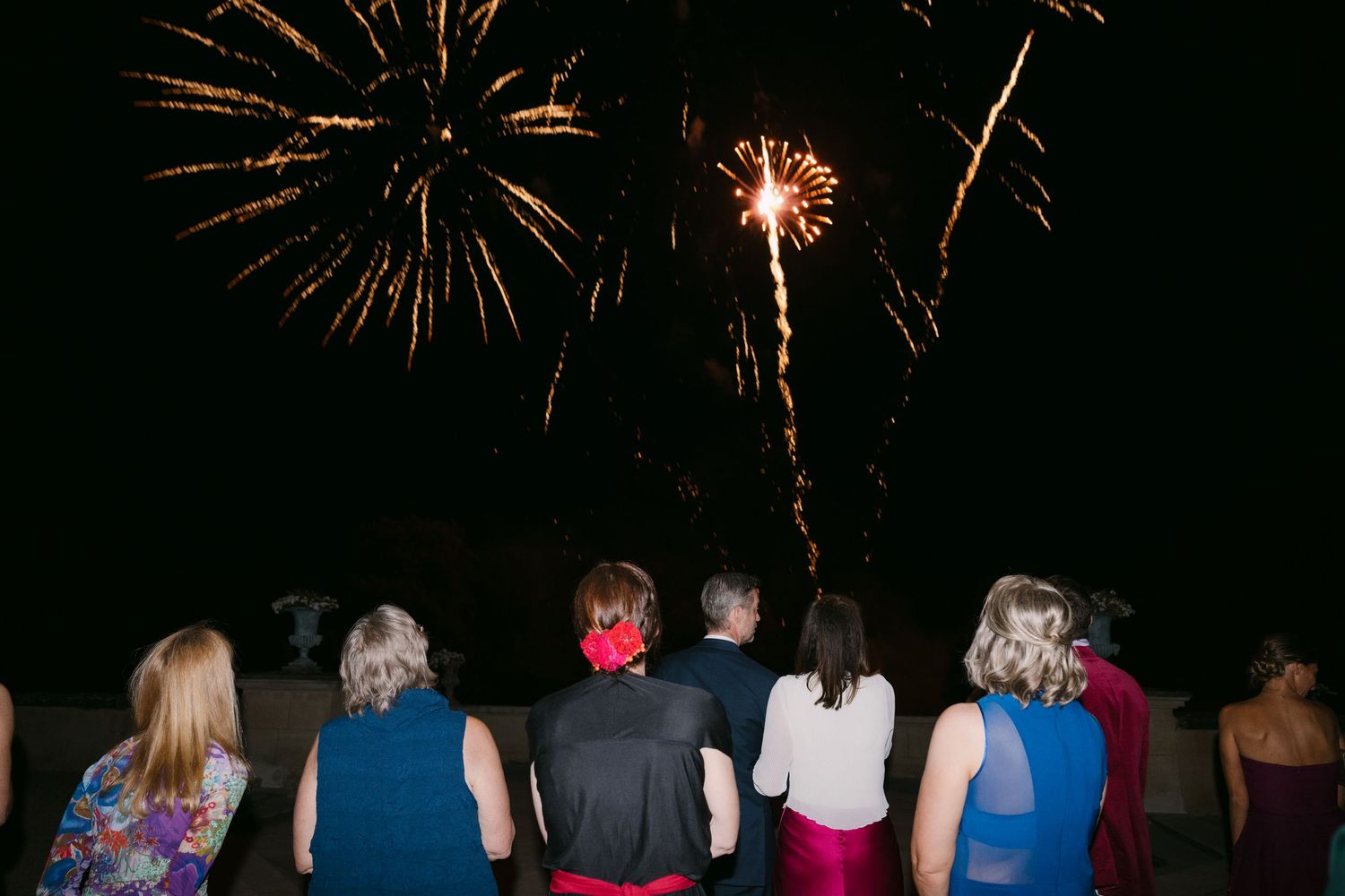 Wedding guests watching a colorful fireworks display light up the dark night sky.