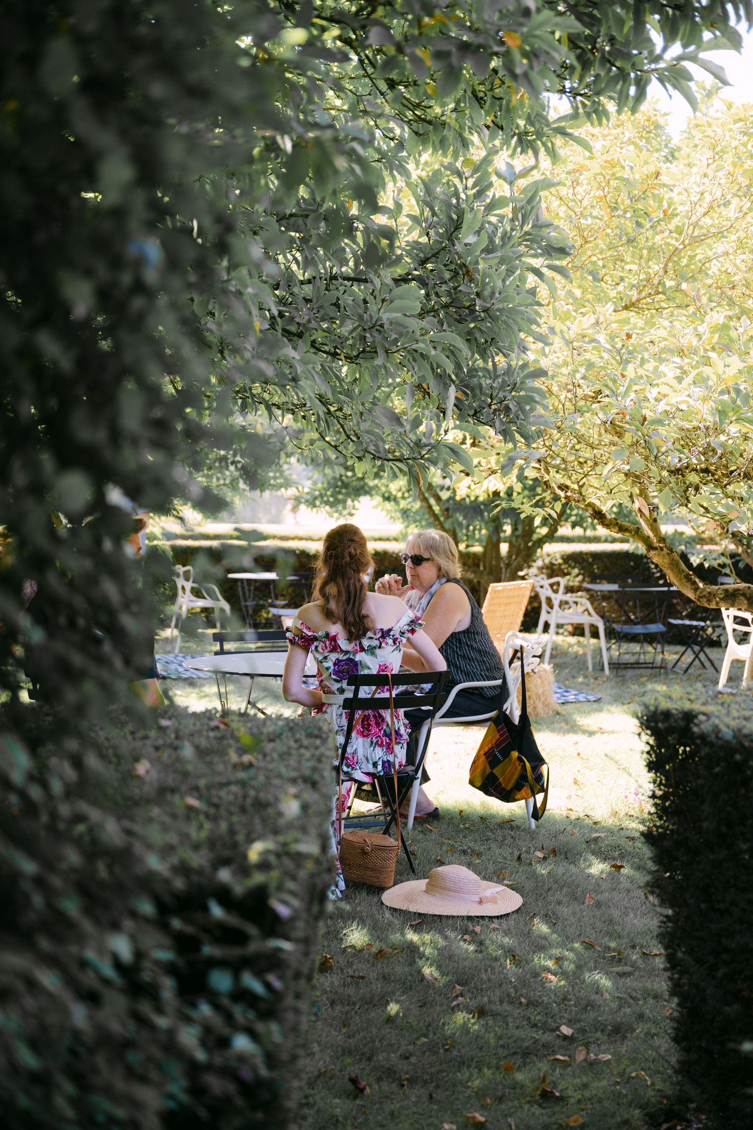 Two women sitting at an outdoor garden table beneath leafy trees at a French estate venue.