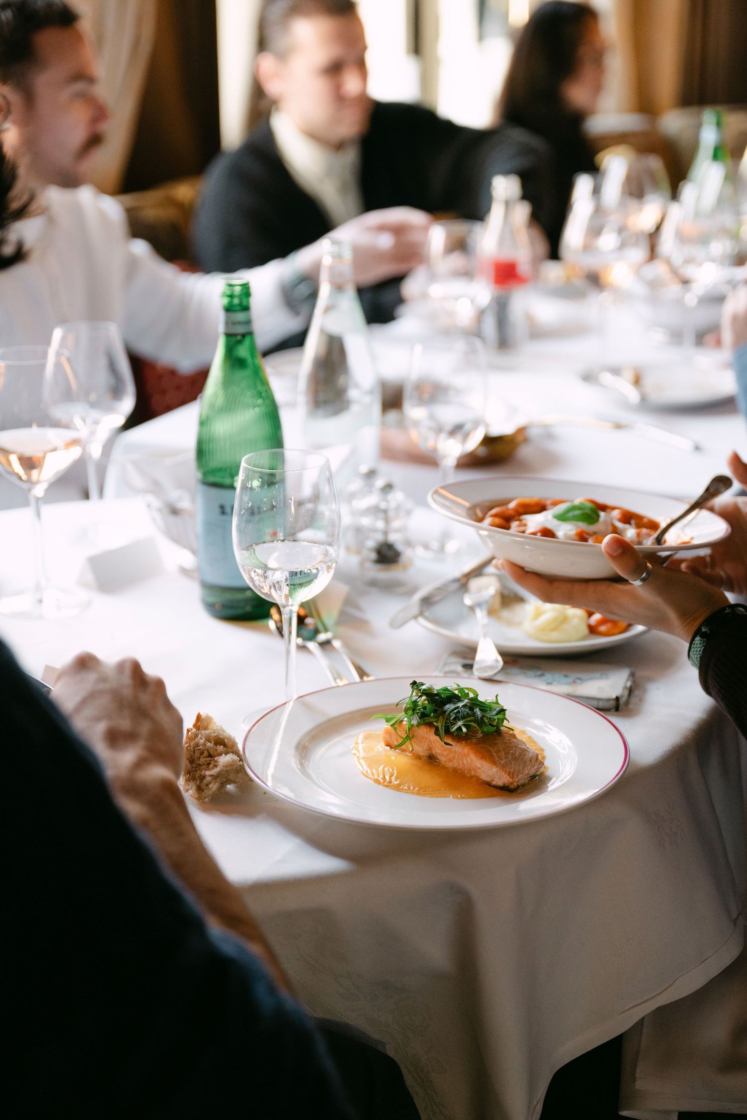 Fine dining table setting with salmon dish, wine glasses and San Pellegrino water.