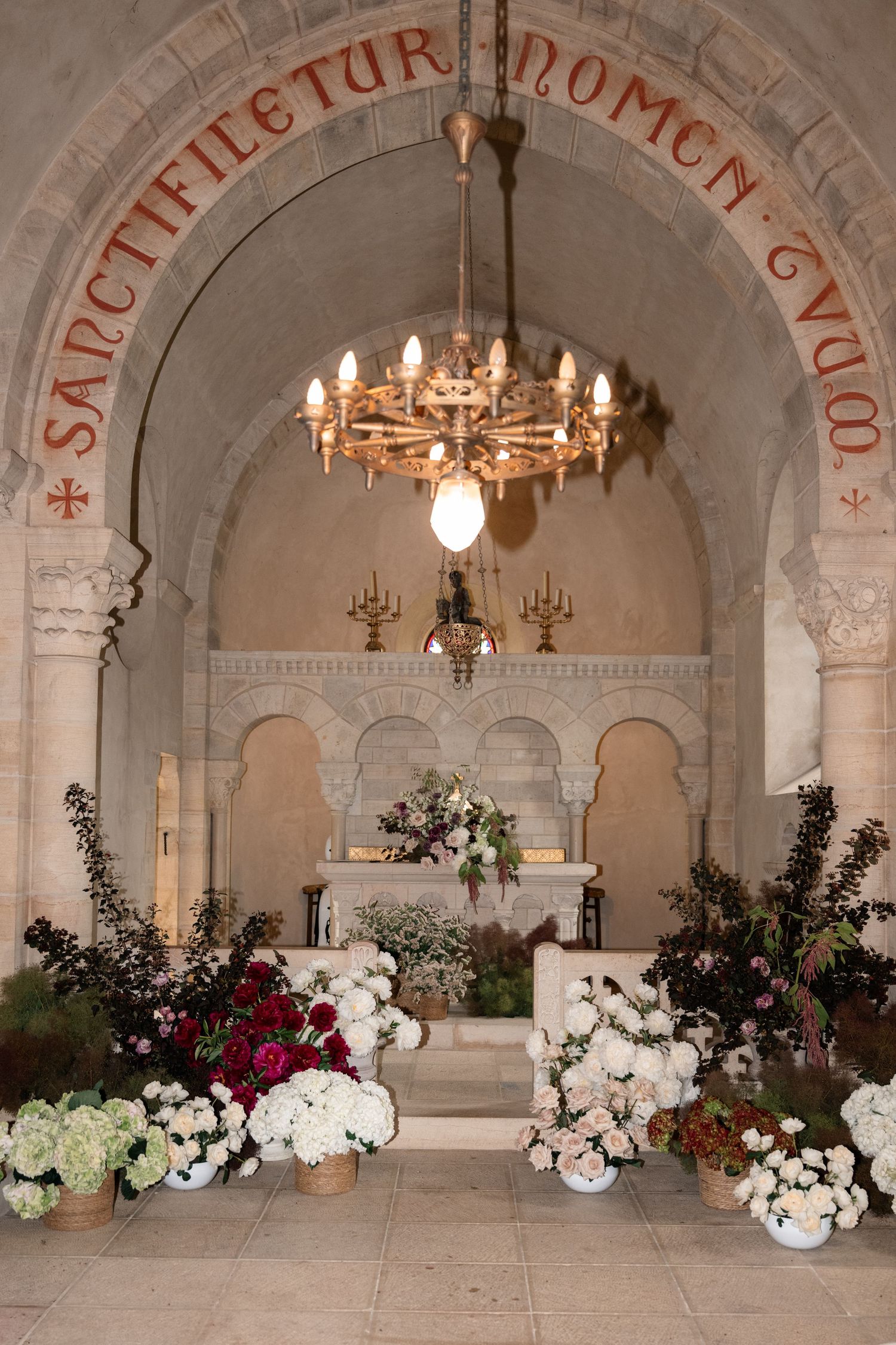 Elegant stone archway decorated with white and red floral arrangements and illuminated by ornate chandeliers.