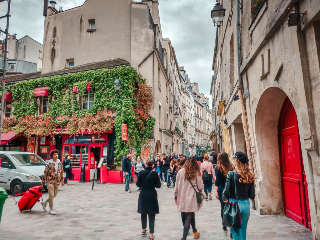 Bustling street scene in Paris with ivy-covered restaurant and pedestrians walking.