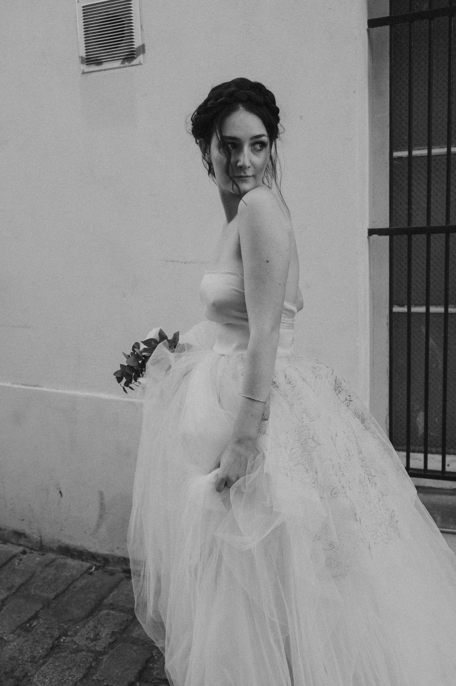 A black and white photograph showing an ethereal wedding dress against a textured wall.