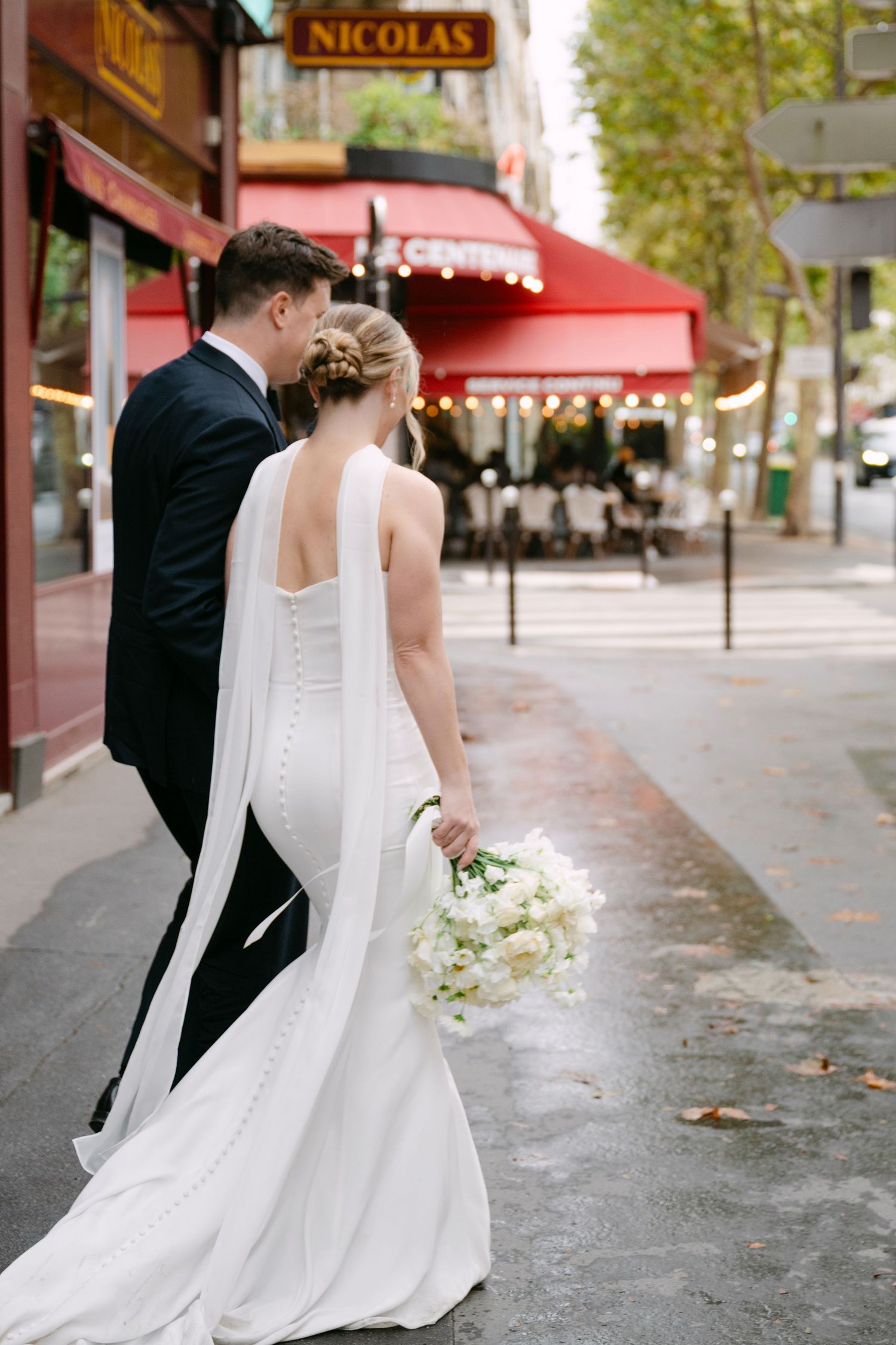 Elegant couple walks along a wet Parisian street with classic red cafe awnings and autumn leaves.