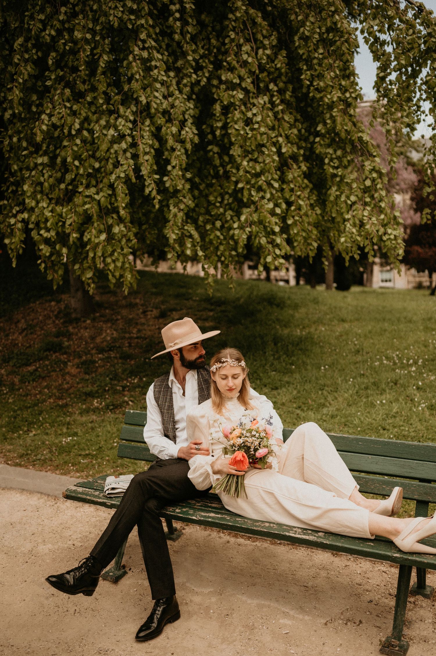 Romantic couple on park bench with flowers beneath drooping willow trees.