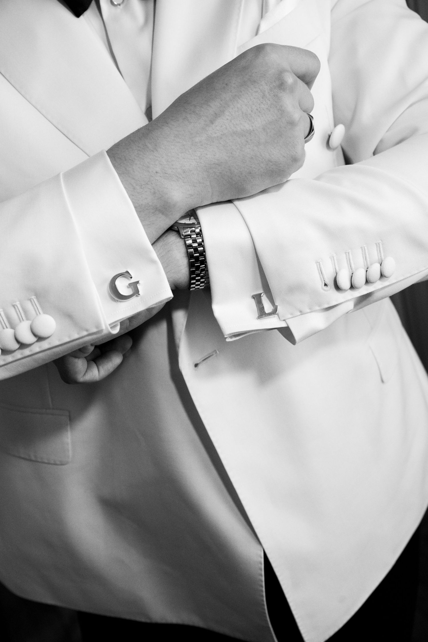 Close-up black and white image of formal attire showing white dress shirt cuffs and dark suit jacket sleeves.