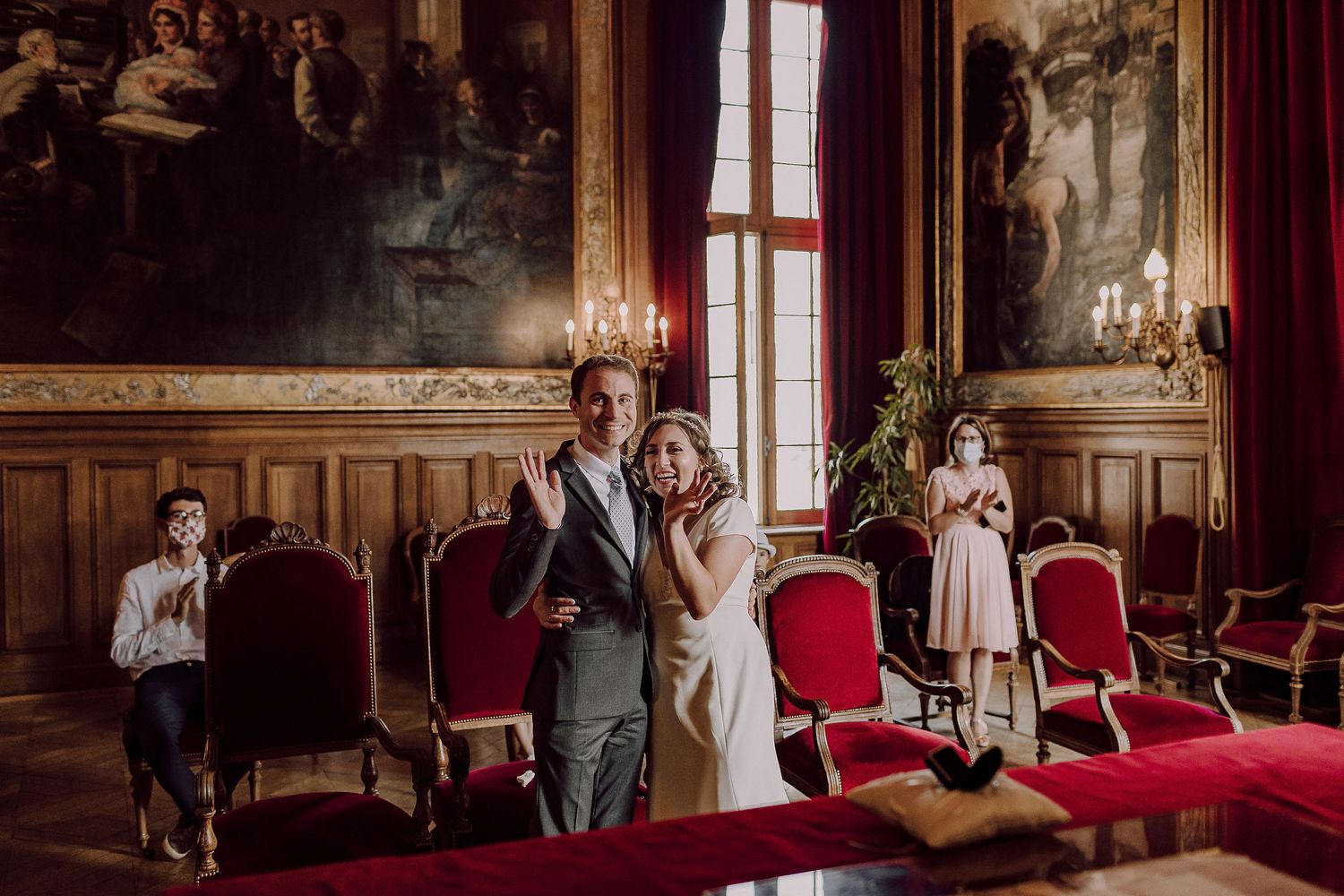 An intimate wedding ceremony in an ornate historic room with red chairs.