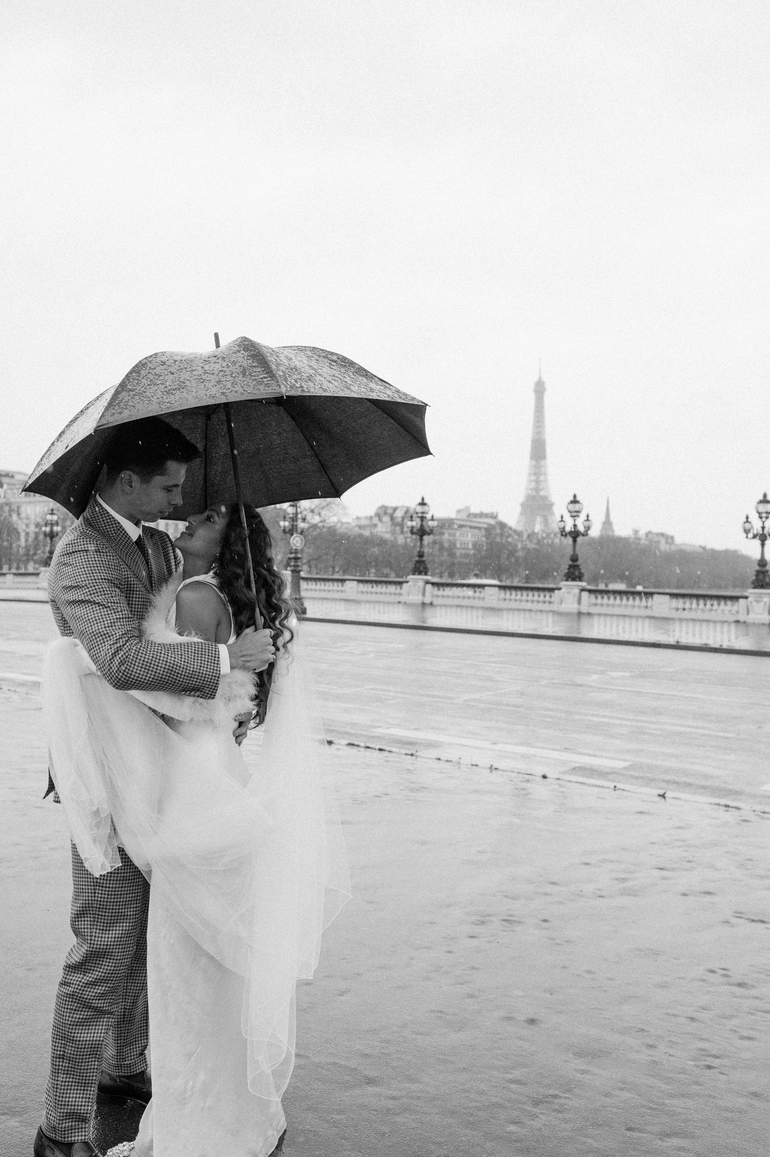 Couple in wedding attire share intimate moment with Eiffel Tower visible in distance.