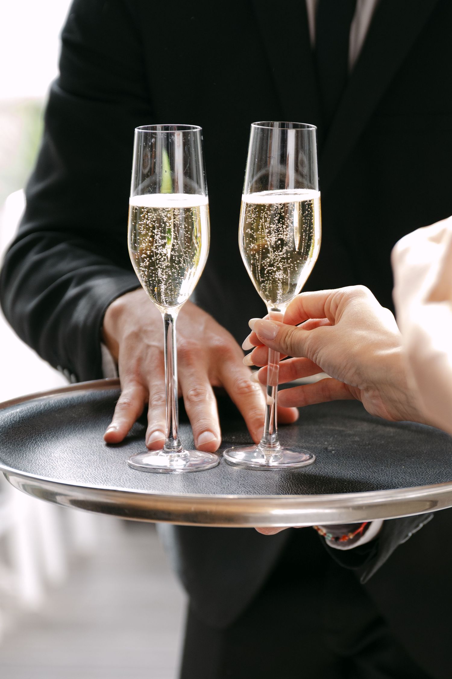 Server carries champagne flutes filled with sparkling wine on a silver tray at an elegant event.
