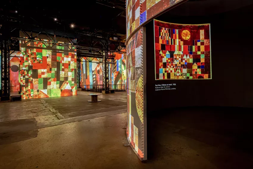 Vibrant digital art installation with geometric patterns and colorful light projections in dark gallery space.