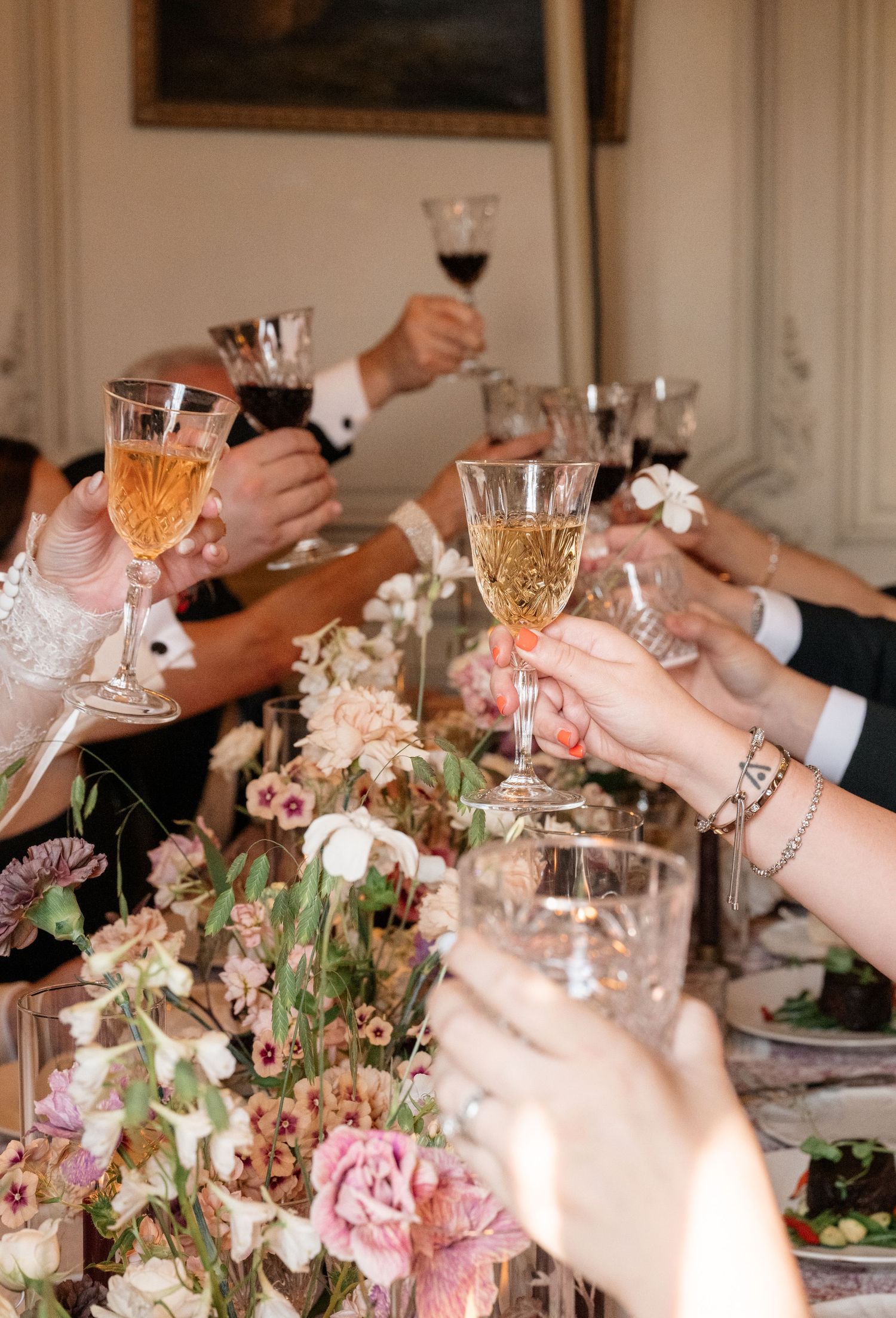 Wedding guests raising crystal glasses in a toast at an elegant dining table adorned with pink floral centerpieces.