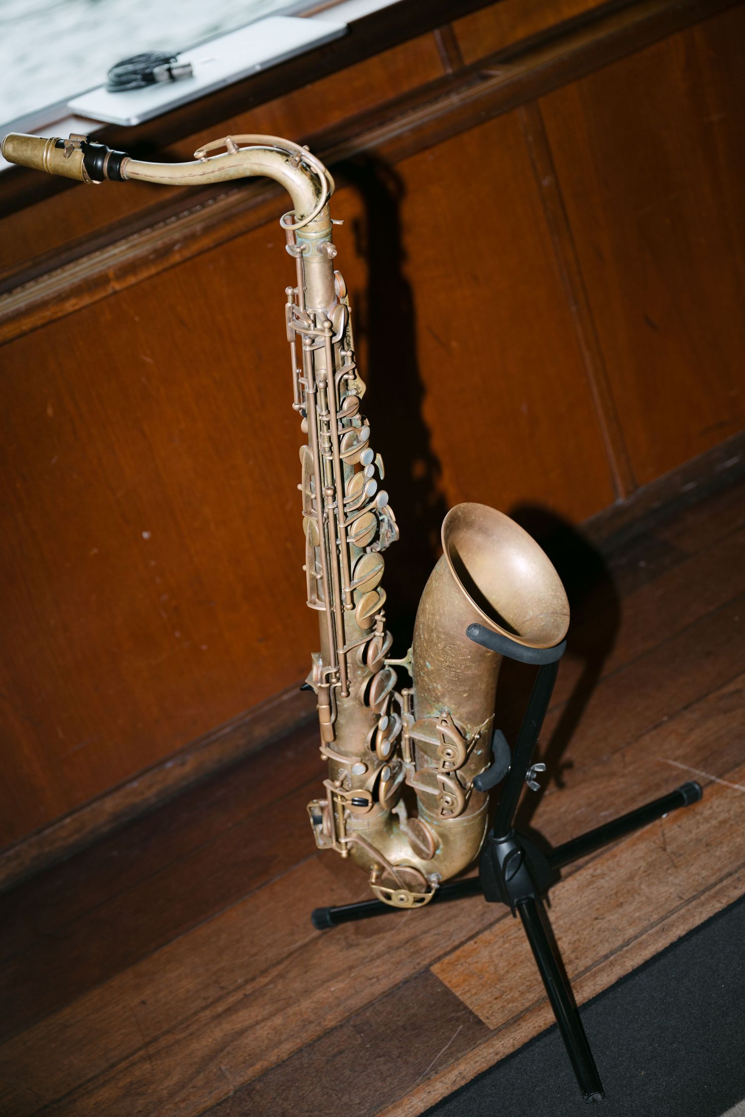 A gold saxophone rests on dark wooden floorboards with dramatic lighting.