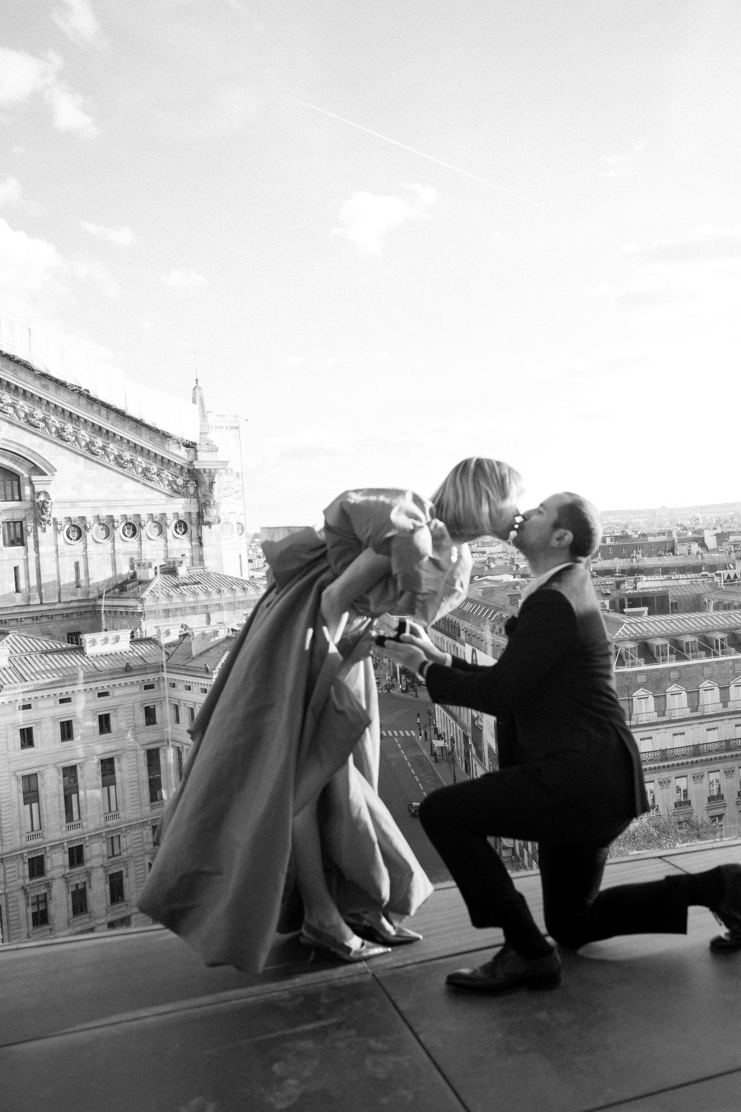 Black and white proposal photo on Parisian rooftop with city skyline in background.