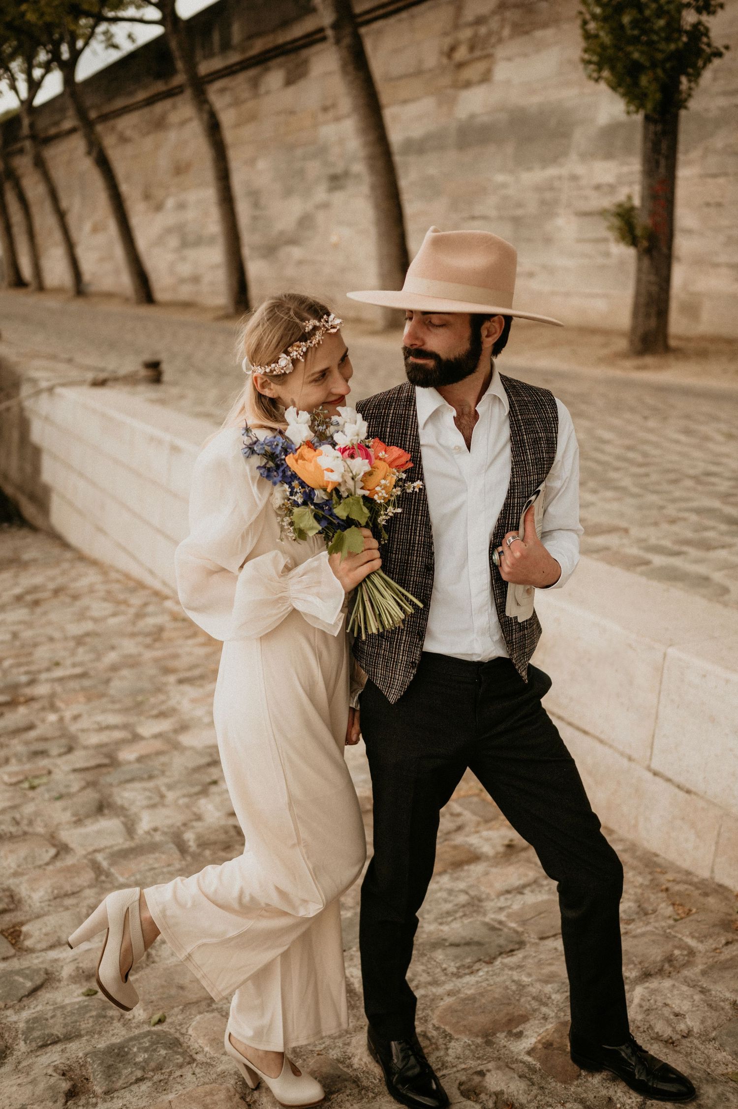 A candid moment of newlyweds dancing on cobblestone streets with a vibrant floral bouquet.