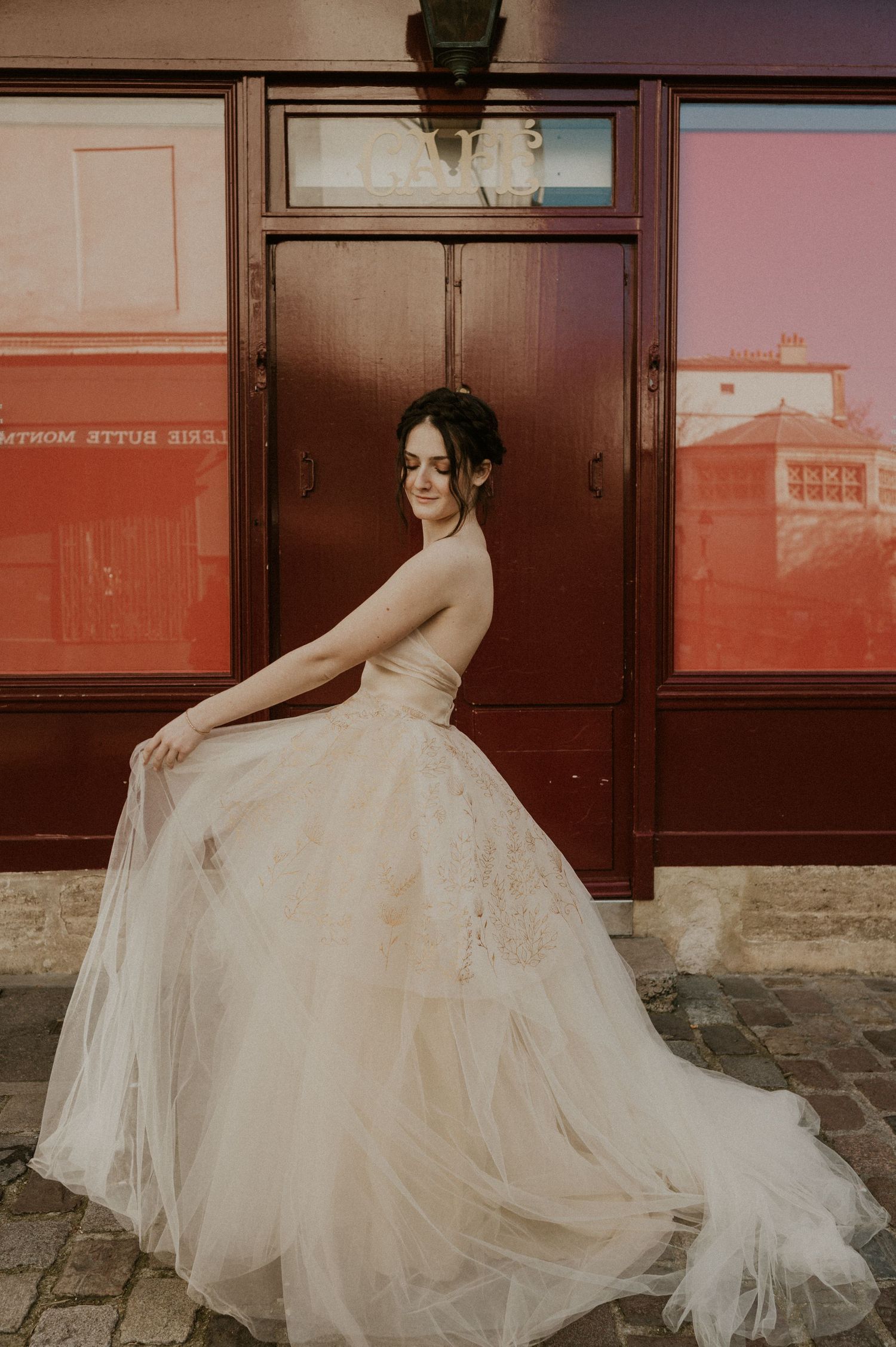 A bride in a flowing tulle wedding gown poses gracefully against a rustic red doorway.