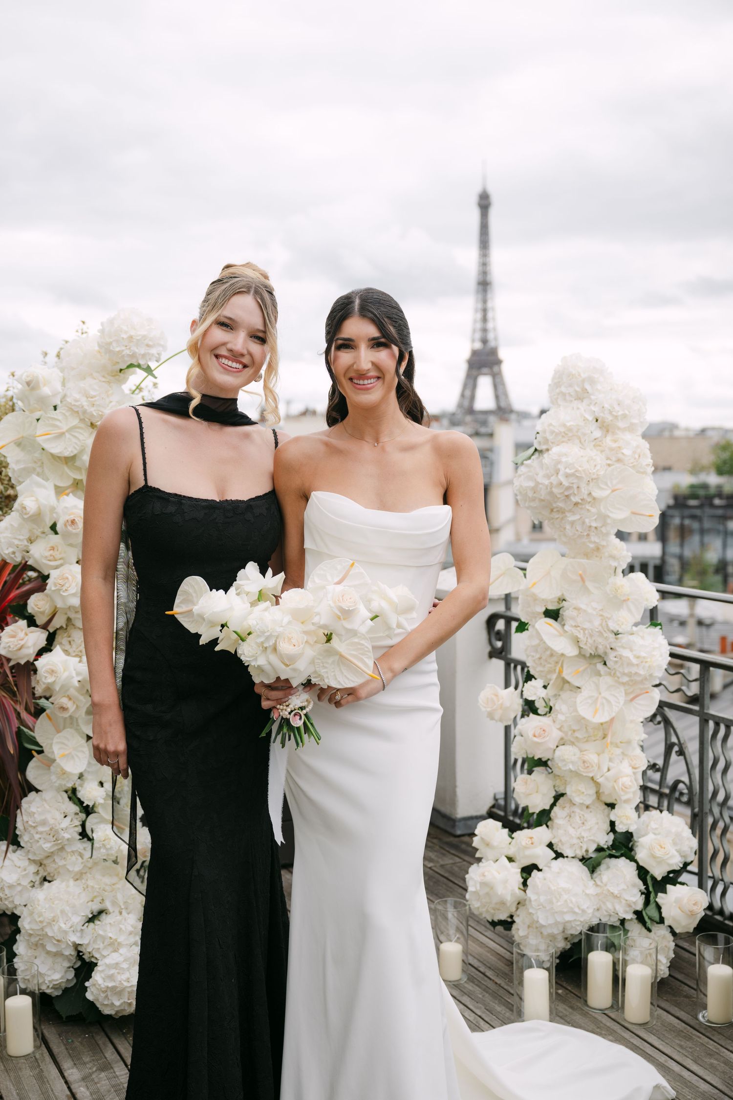 Bride in white strapless gown and bridesmaid in black dress pose with Eiffel Tower backdrop in Paris.