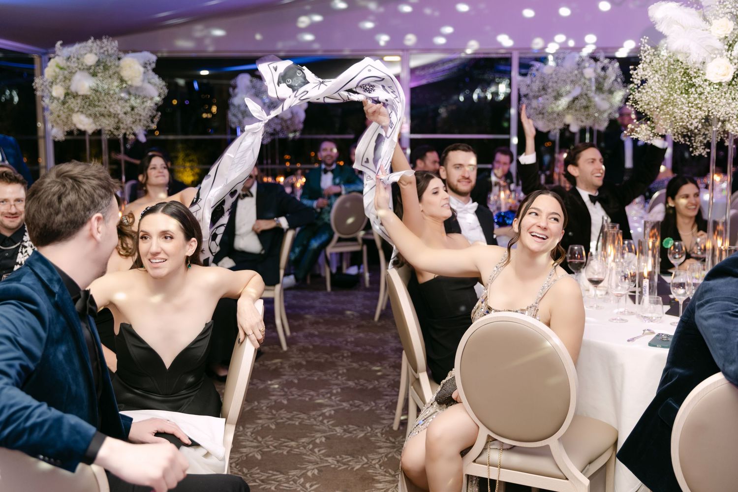 Bridesmaids in black dresses laughing and waving ribbons at festive wedding reception.