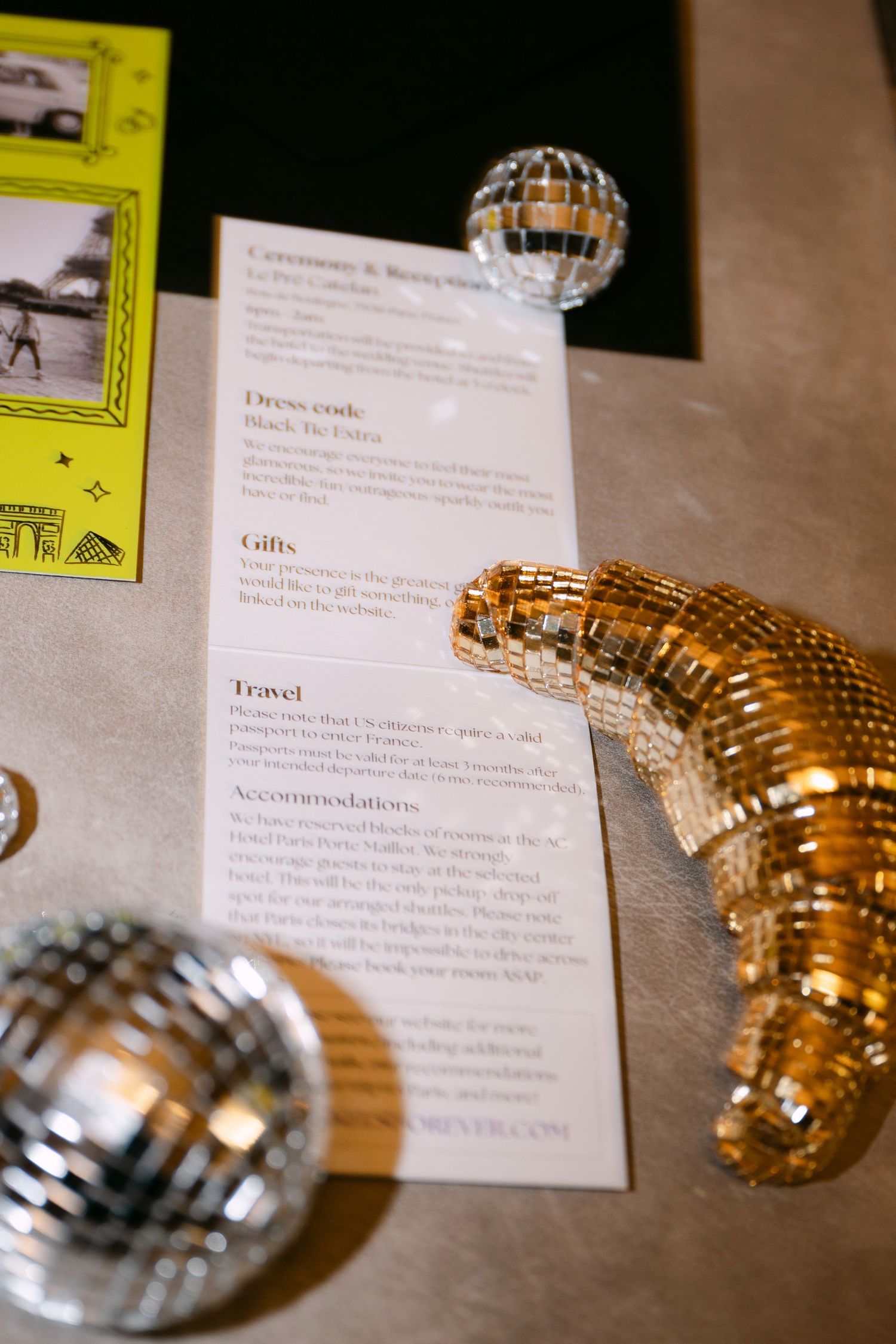 Wedding invitation with disco ball decorations showing dress code and travel details on metallic surface.