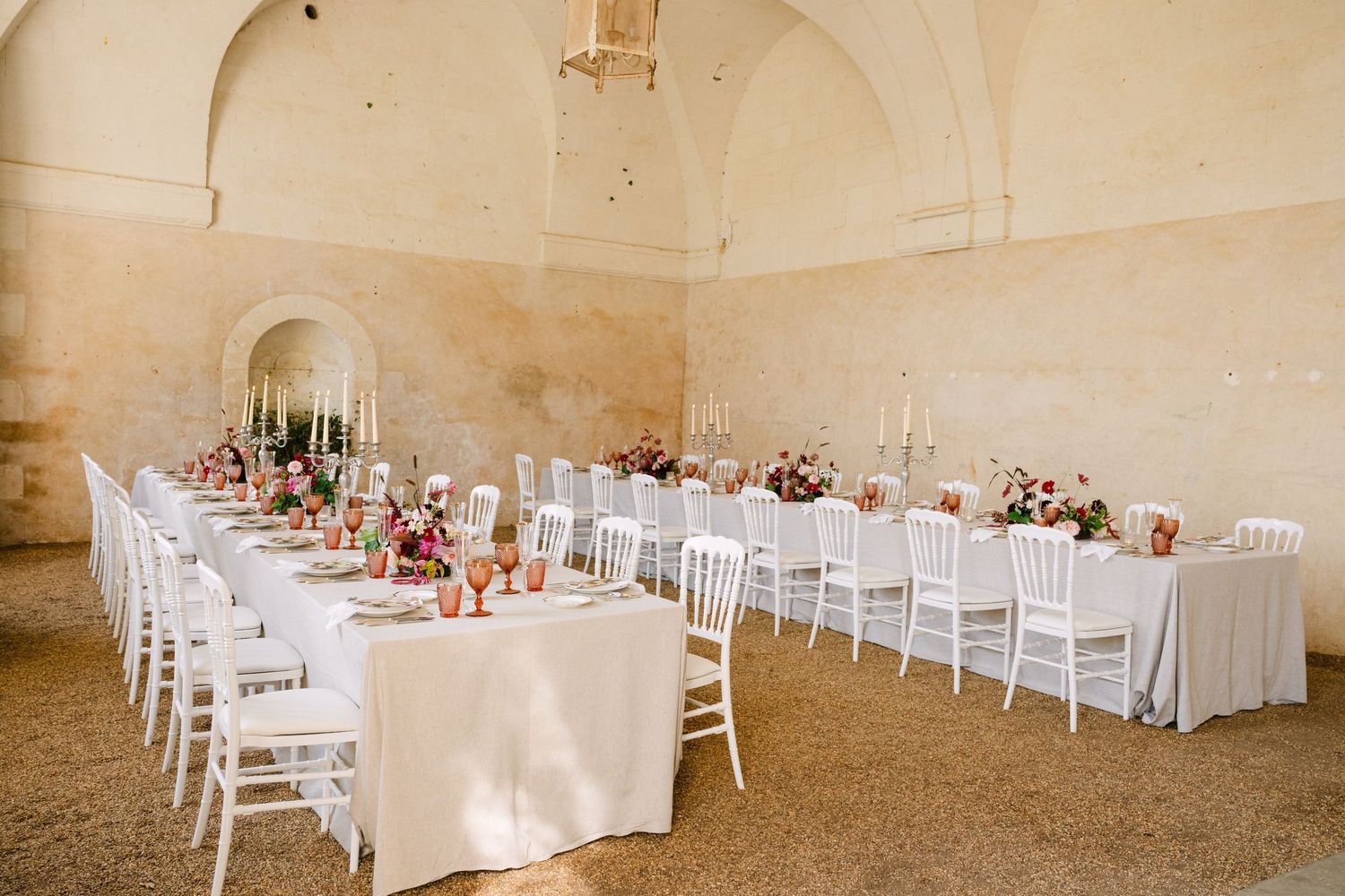 Elegant wedding reception in a stone vaulted hall with long white-clothed tables and colorful floral centerpieces.