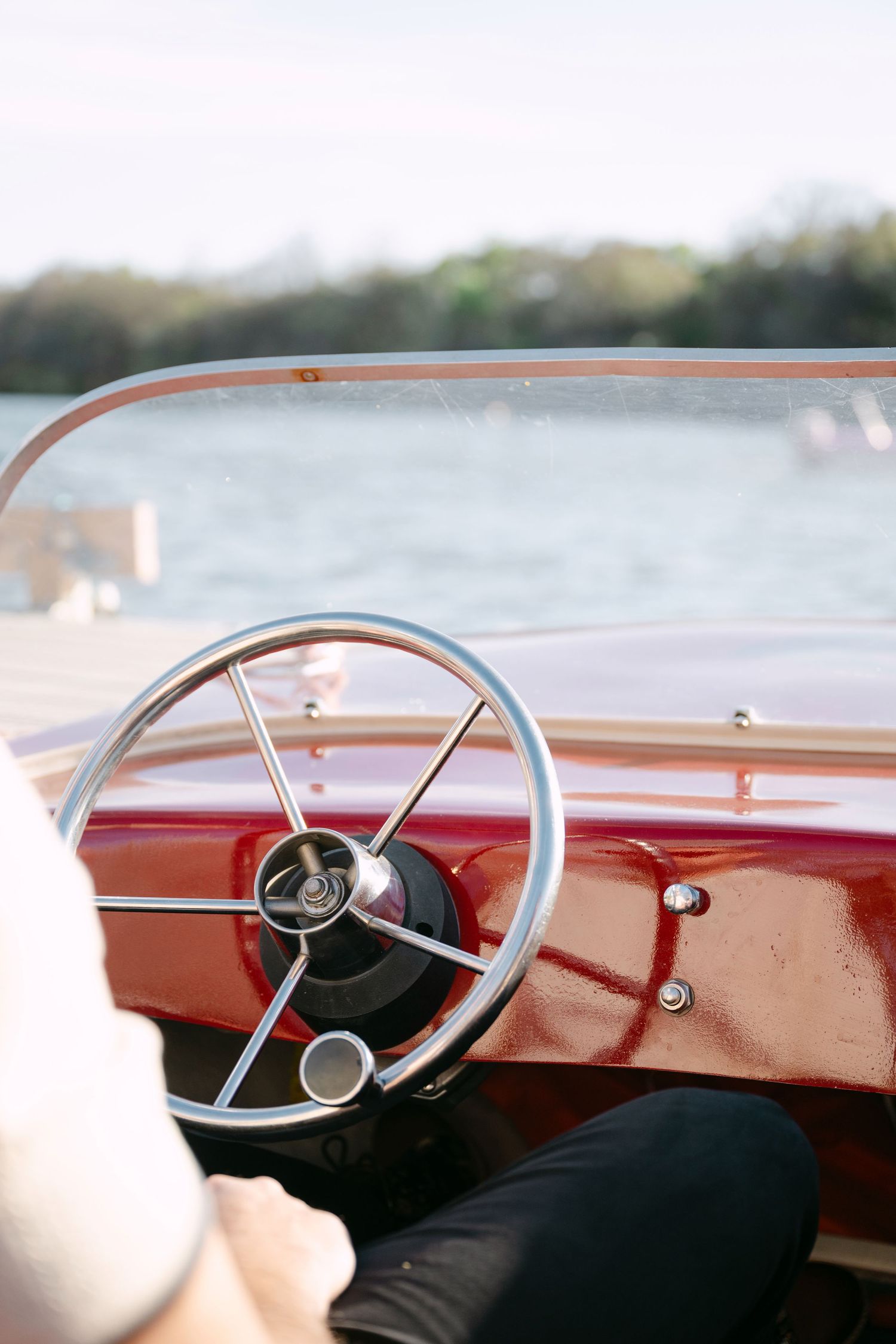 Close-up of vintage red wooden boat steering wheel on sunny day with water visible in background.