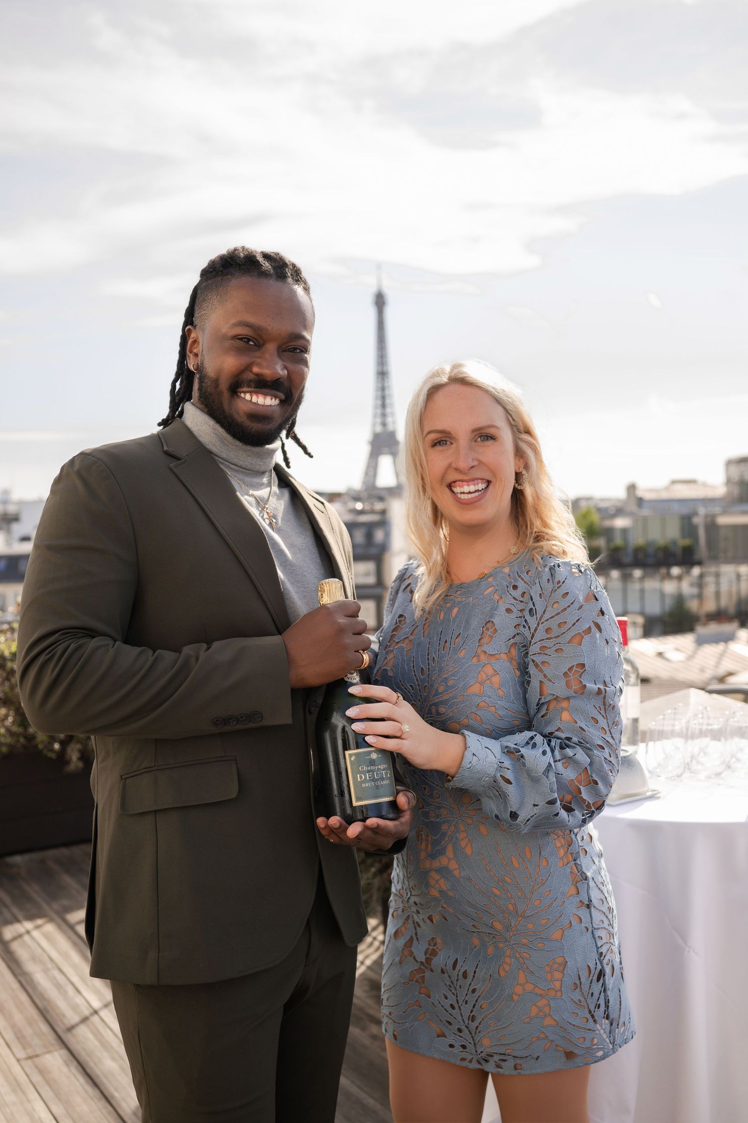 Couple holding a wine bottle on a Paris rooftop with the Eiffel Tower visible behind them.