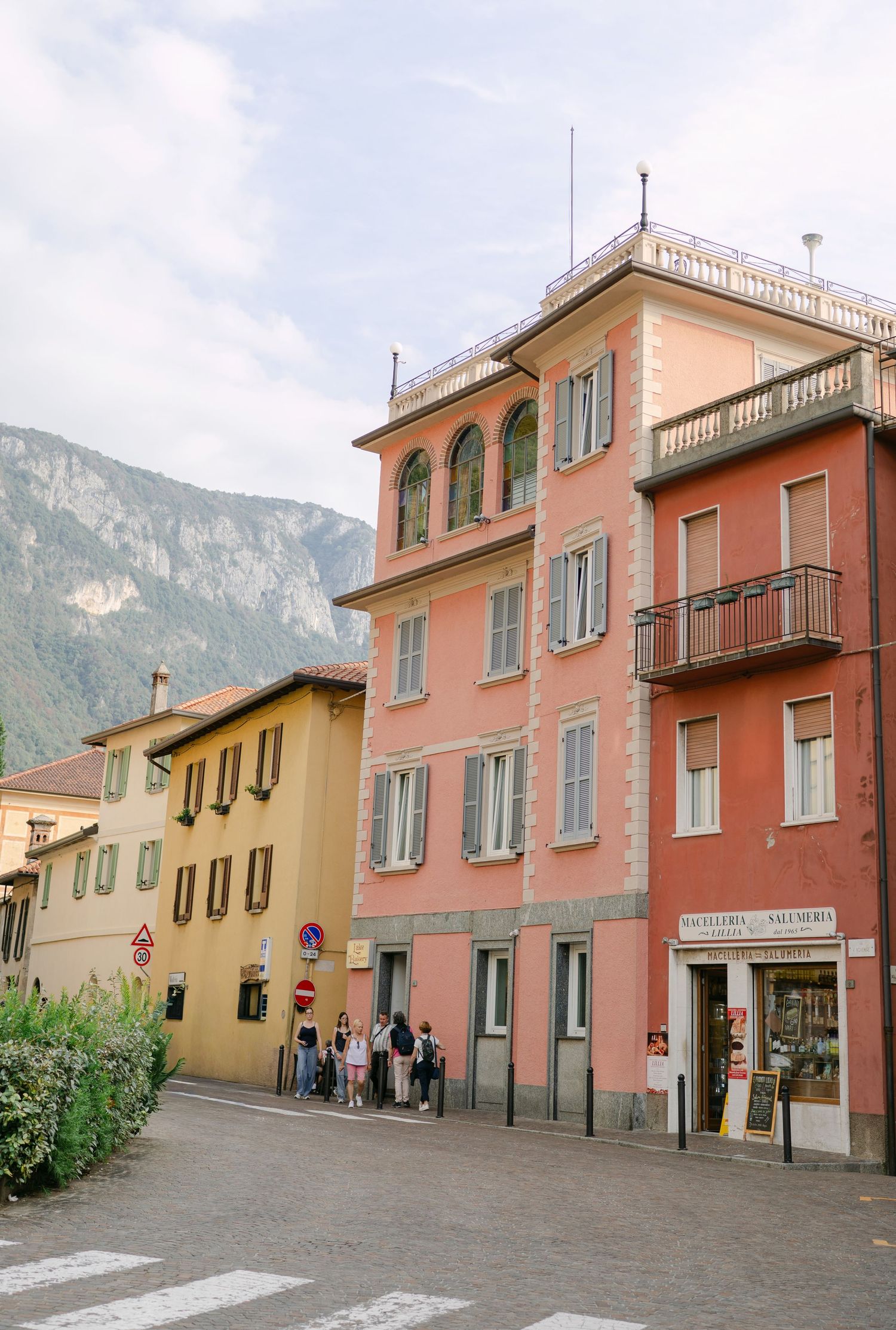 Colorful Italian buildings with pink and yellow facades line a street with mountains in the background.