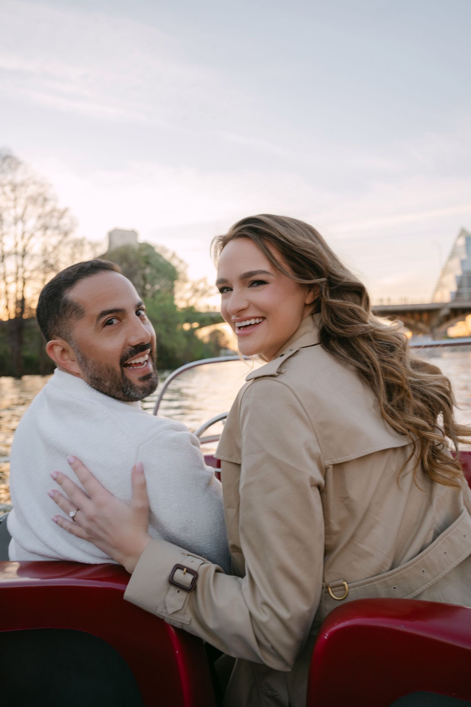 Happy couple embracing and laughing on a red boat at golden hour.