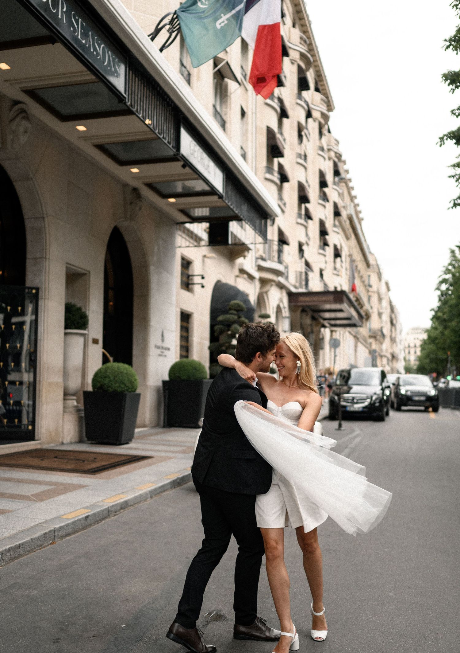 Groom lifting bride in short white wedding dress outside Four Seasons Hotel George V in Paris.