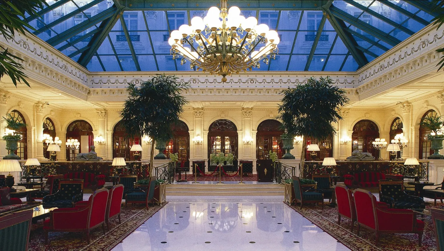 Opulent hotel atrium with crystal chandelier, marble floors and indoor palm trees.