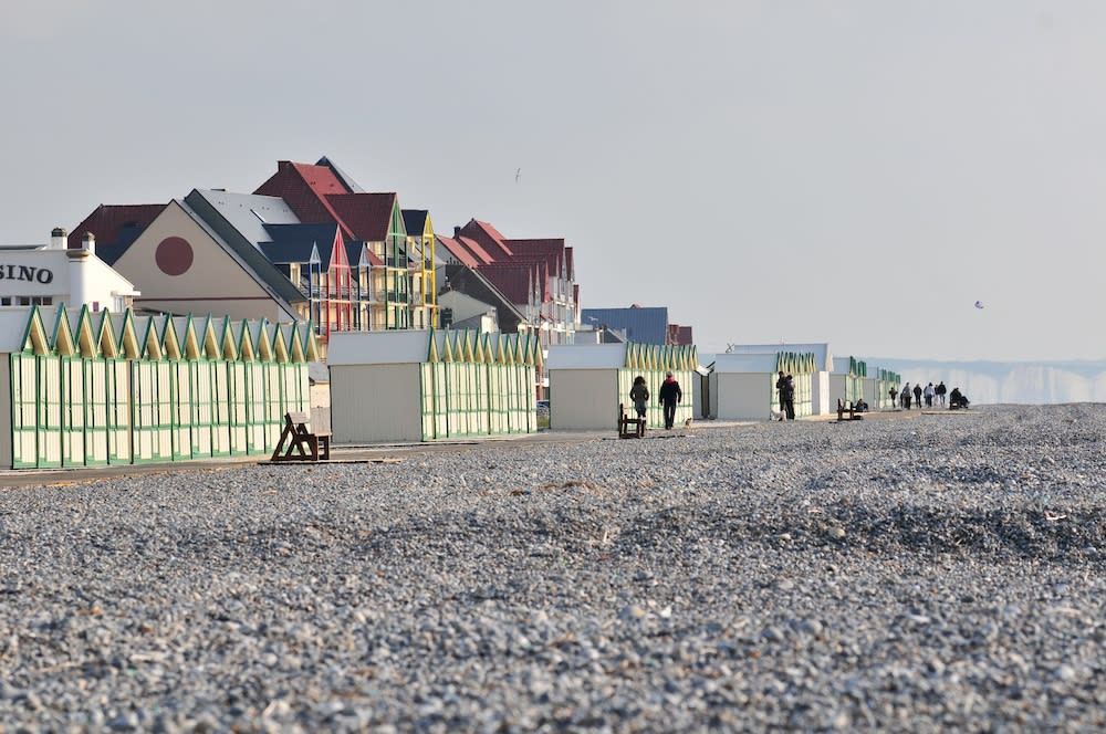 Colorful beach huts line a pebble beach under an overcast sky.