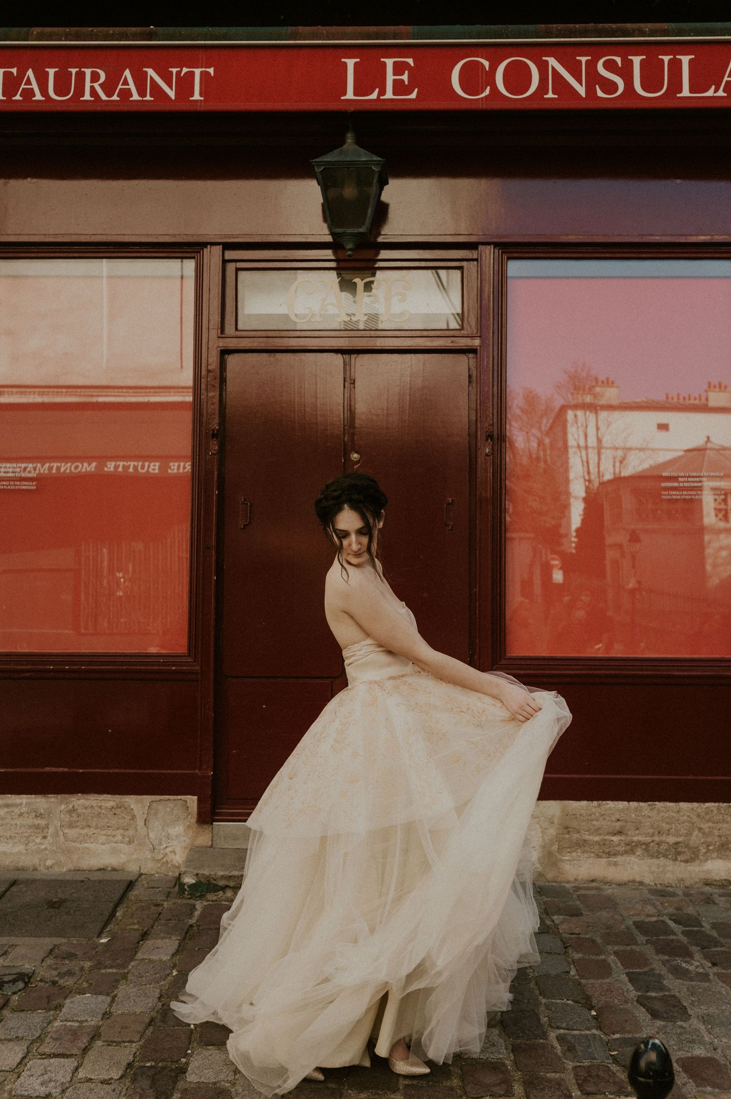 Elegant wedding dress swirling in motion against vintage French restaurant facade.