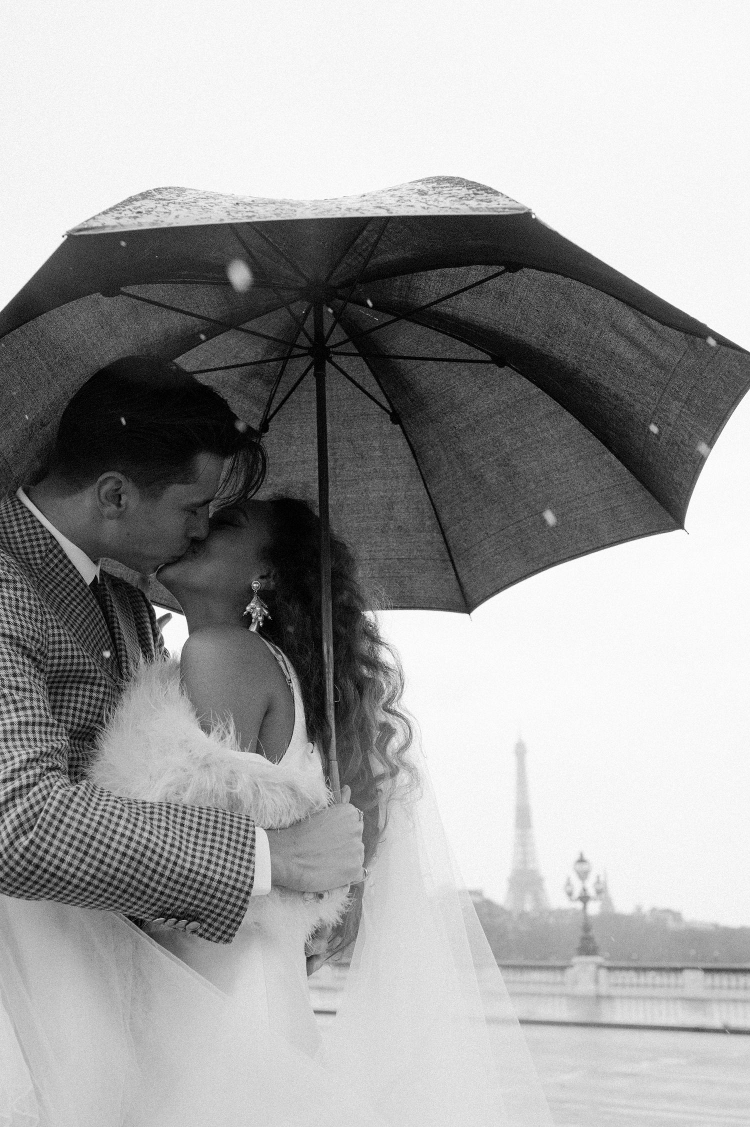 Intimate black and white portrait of couple beneath umbrella with Eiffel Tower in background.