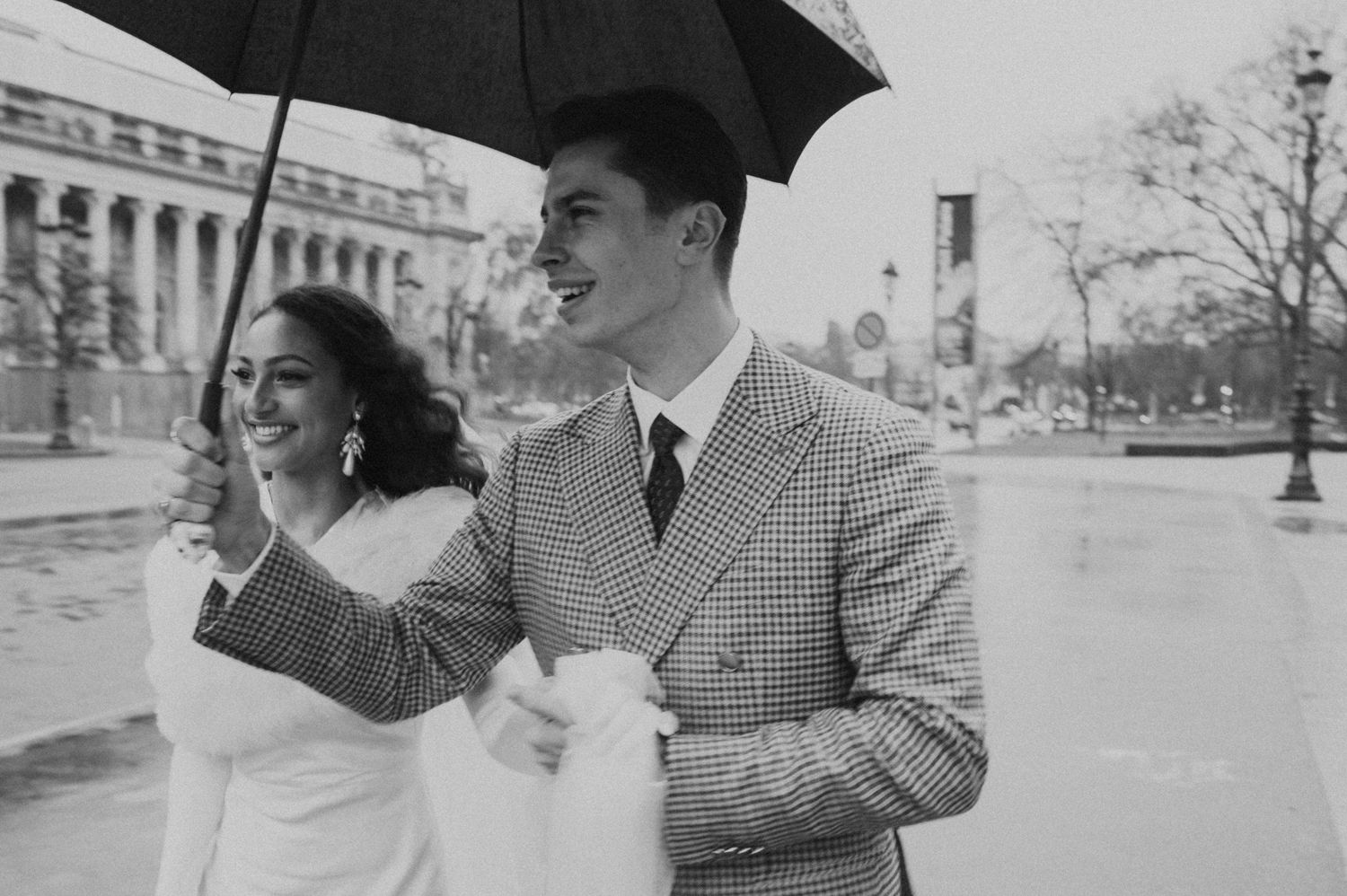 Joyful black and white photo of a couple with umbrella against classical architecture background.
