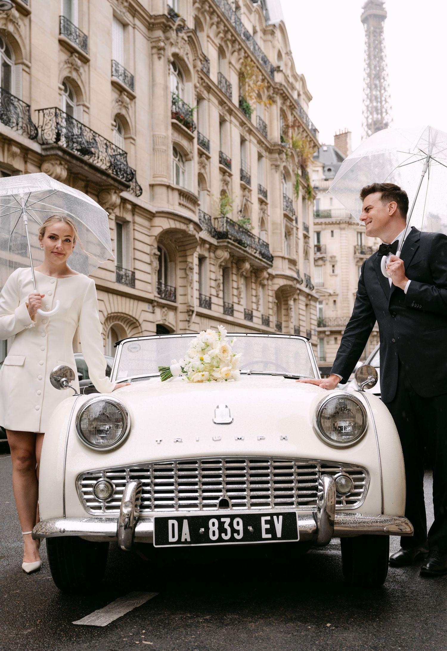 Vintage white classic car parked on a Parisian street with the Eiffel Tower visible in the background.