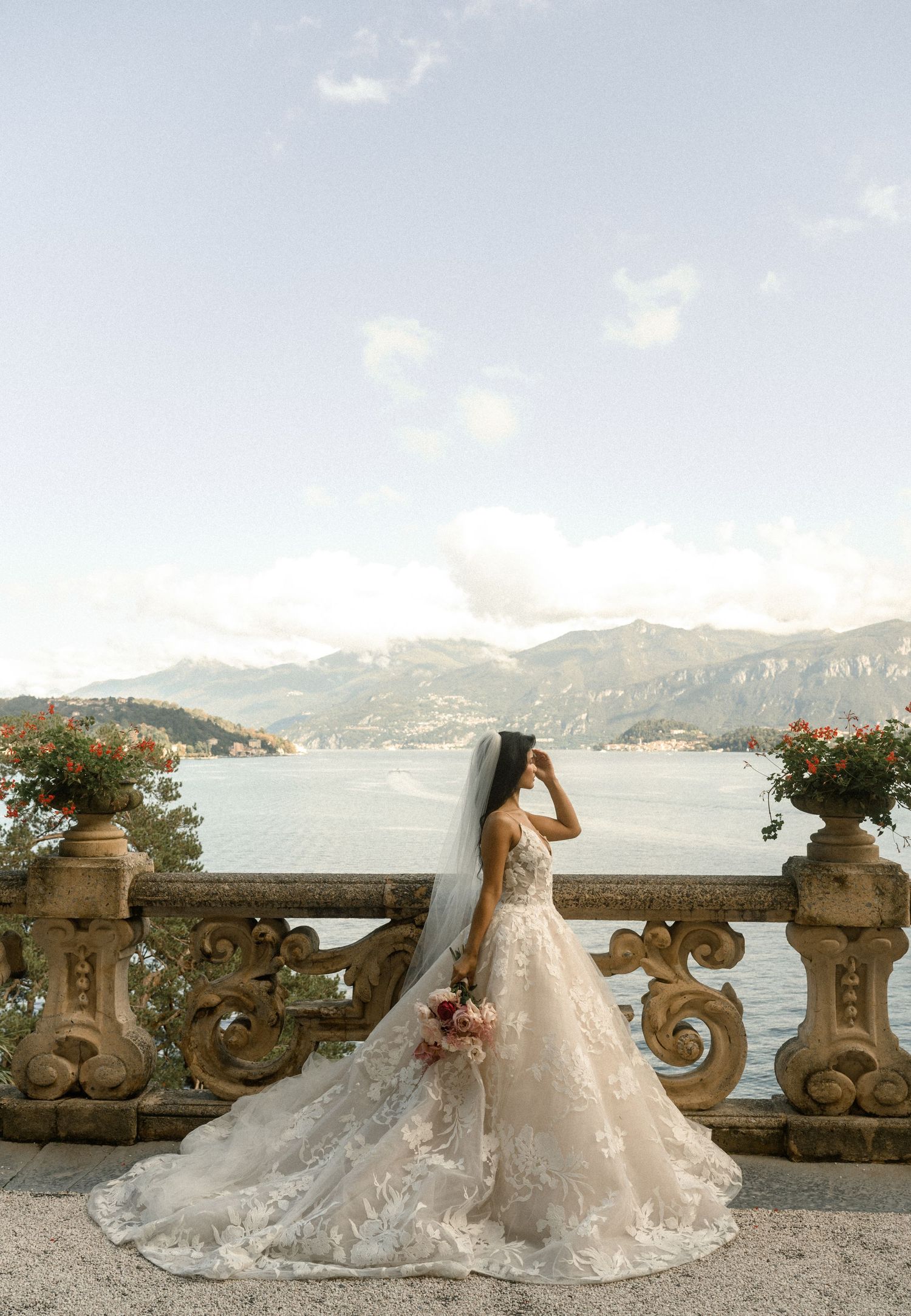 Scenic lake and mountain view from an ornate stone balcony with decorative floral arrangements.