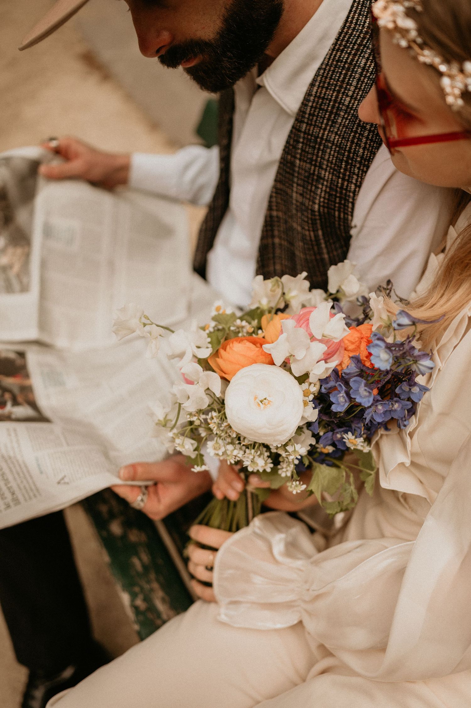 Intimate close-up of hands holding a newspaper beside a vibrant bouquet with white and coral flowers.