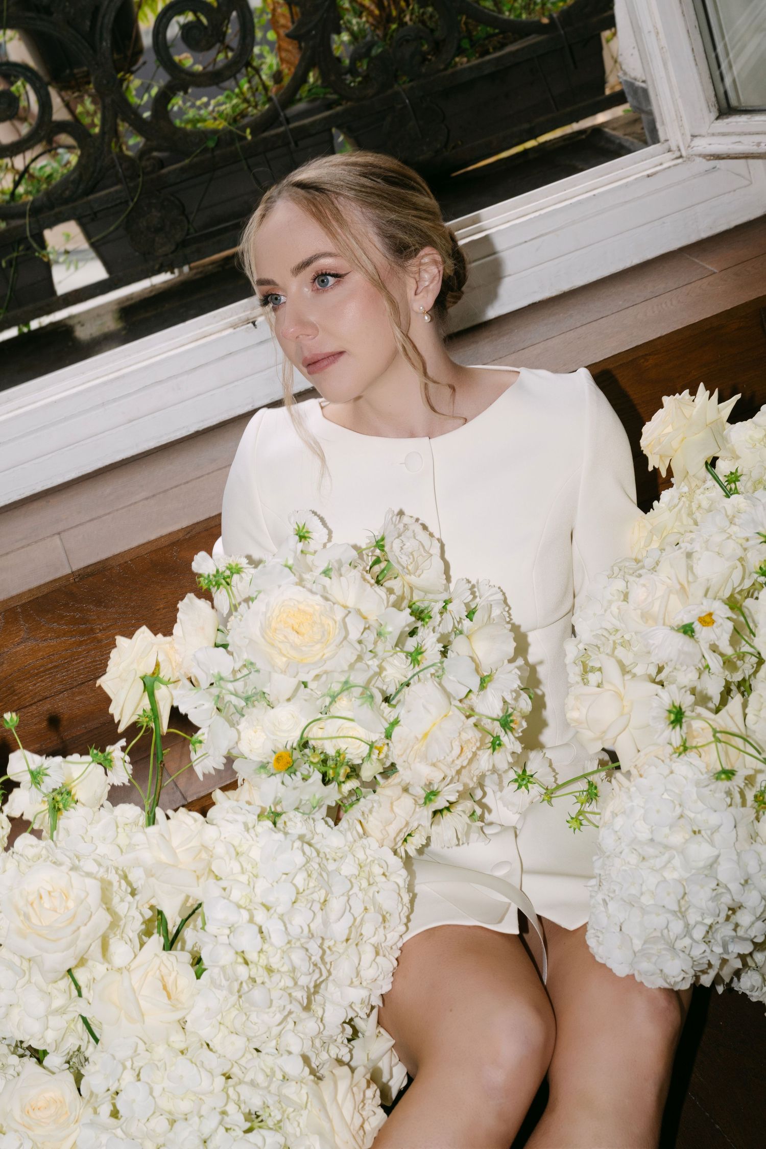 Elegant white floral arrangement with roses and hydrangeas sits beside someone in a white long-sleeved dress.