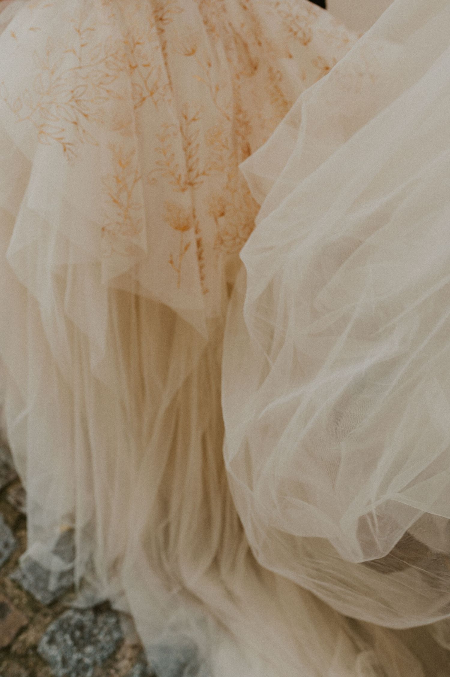 Detailed shot of cream-colored tulle and embroidered wedding dress fabric against stone.