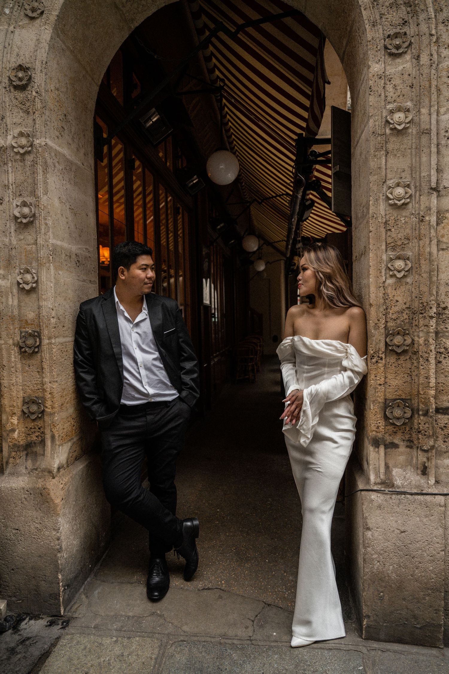 Elegant couple poses in historic stone archway wearing formal attire.