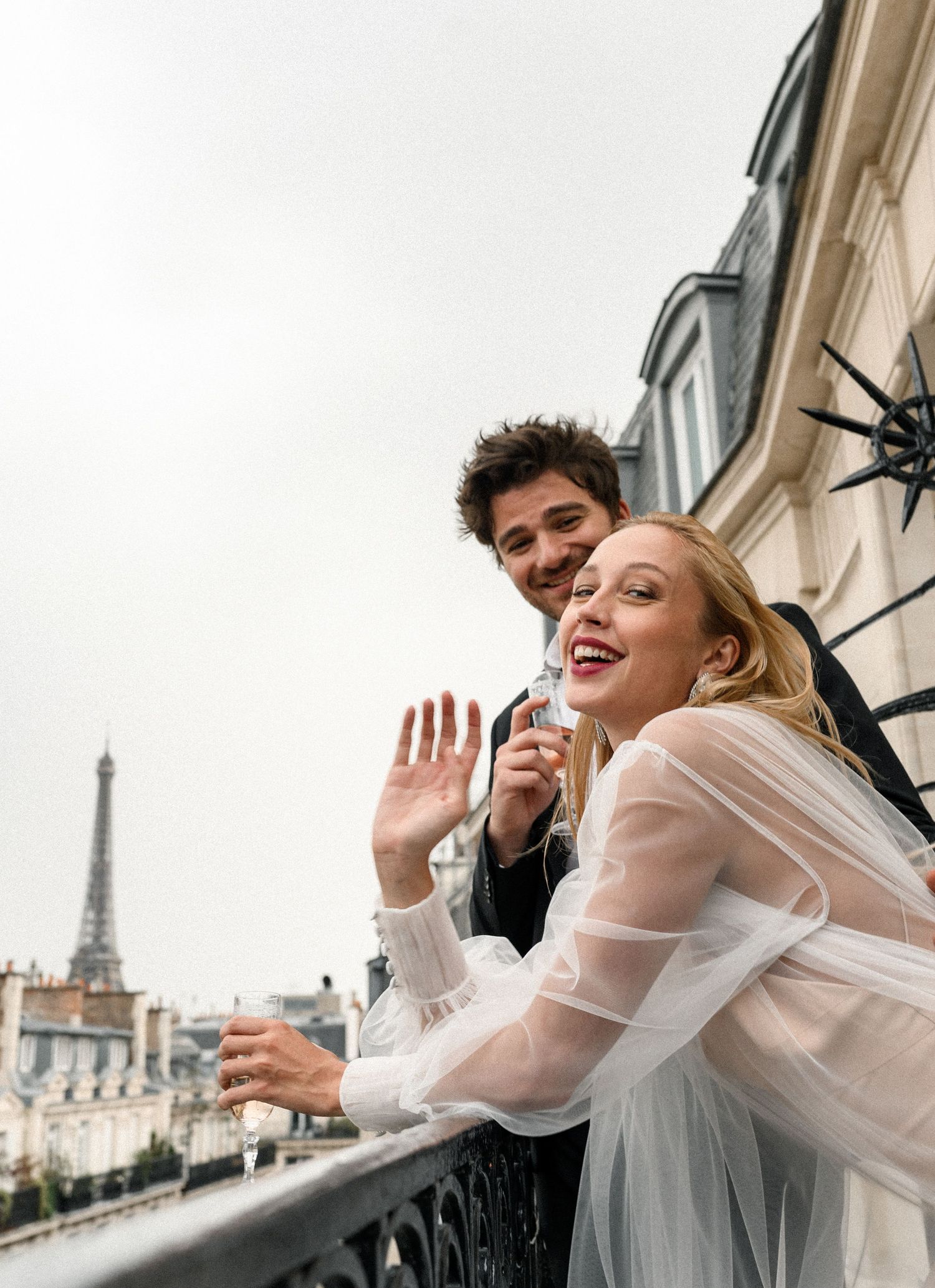 Smiling newlyweds on a Parisian balcony with the Eiffel Tower visible in the background.