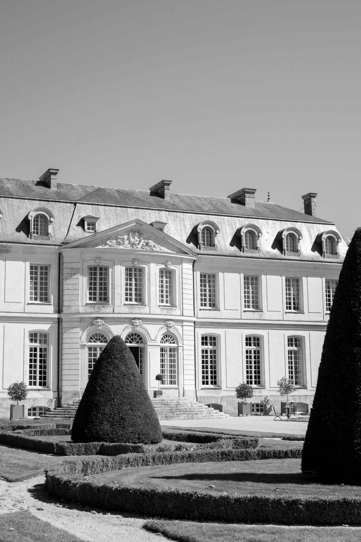 Black and white photo of a classic French chateau with manicured topiary gardens.