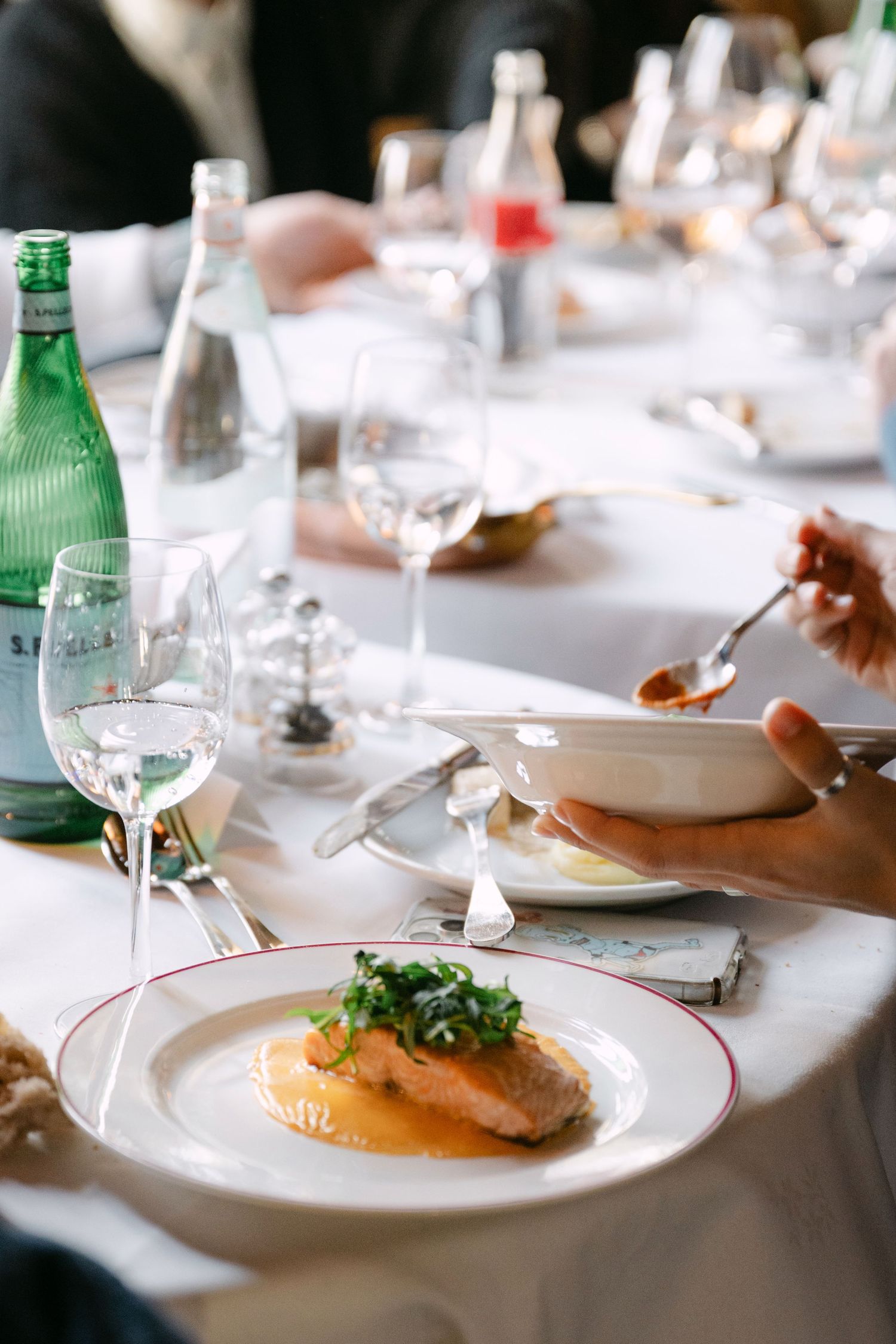 Elegant fine dining plate with salmon and microgreens on white tablecloth with wine glasses.