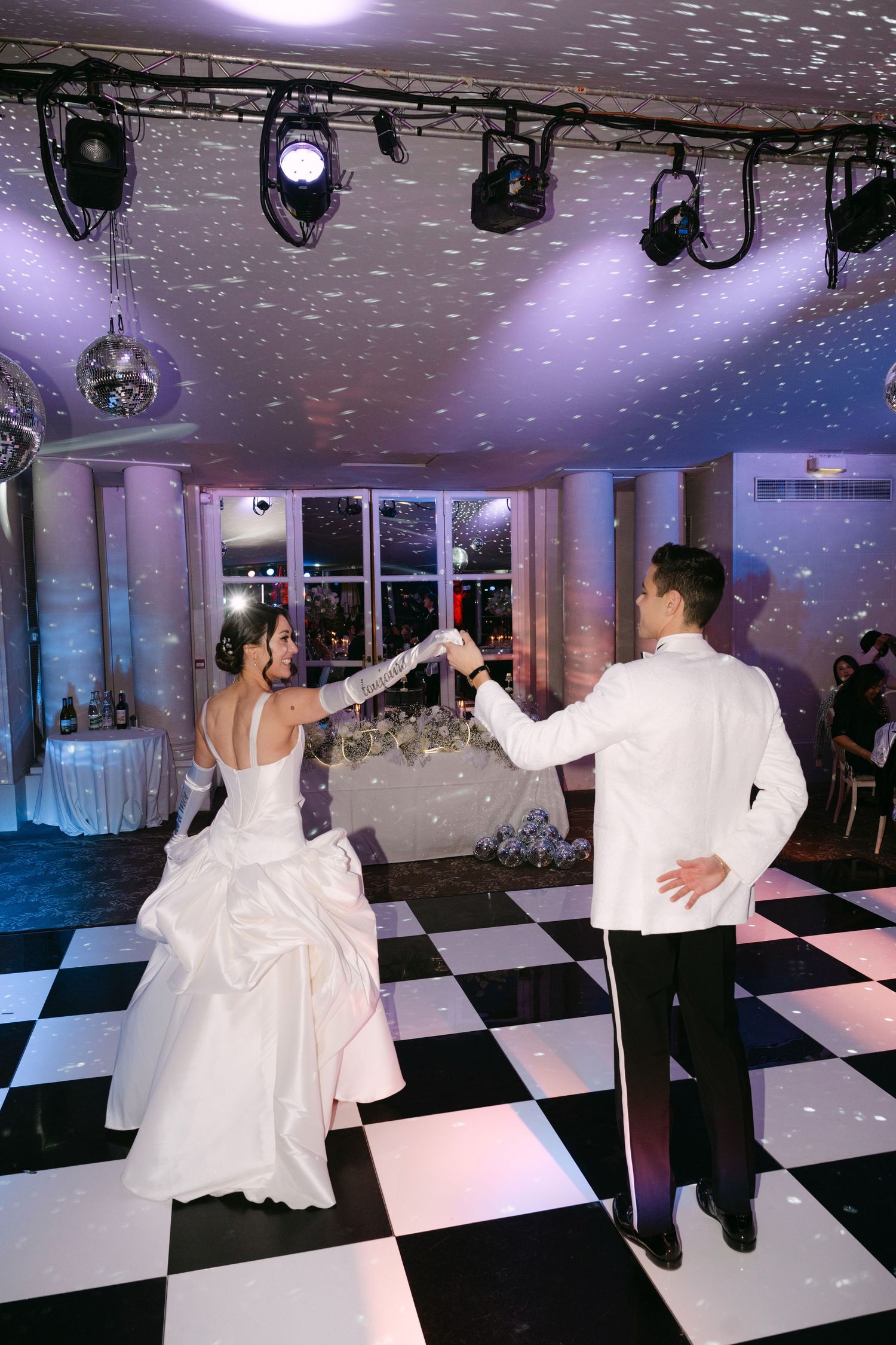 Bride and groom twirl together on a checkered dance floor under stage lights and disco balls.