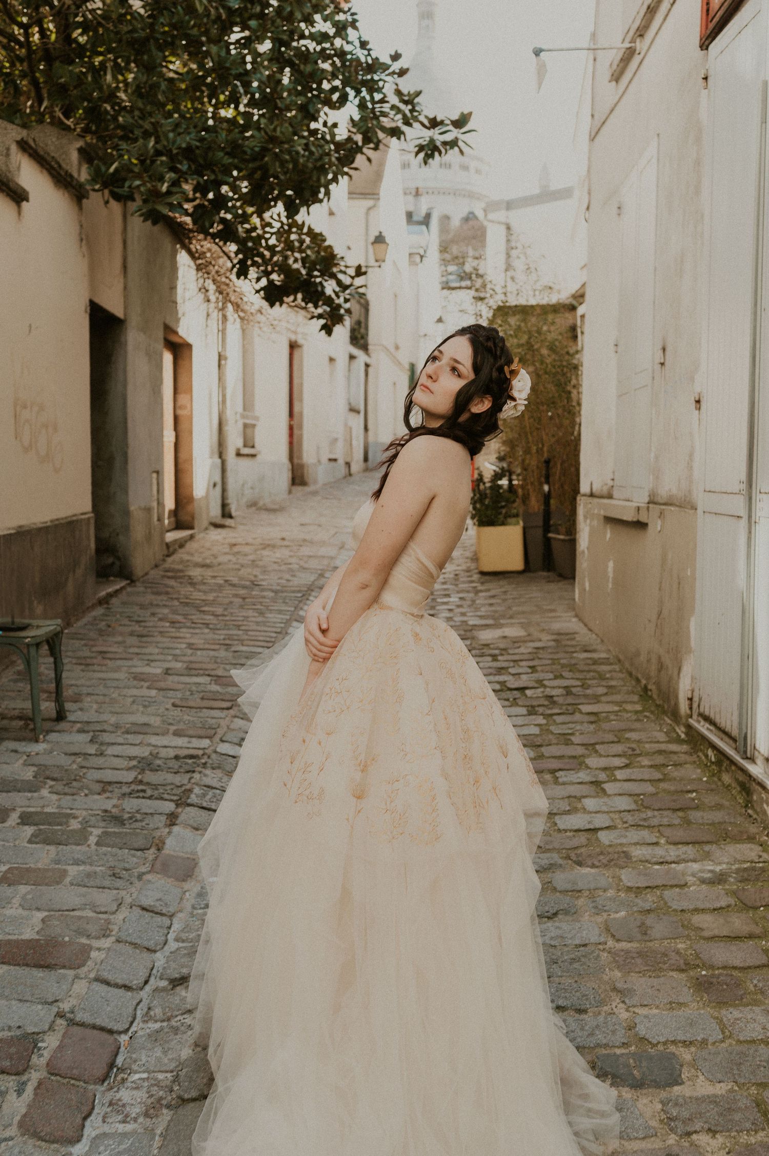 A bride in a layered tulle gown poses gracefully in a sunlit European alleyway.