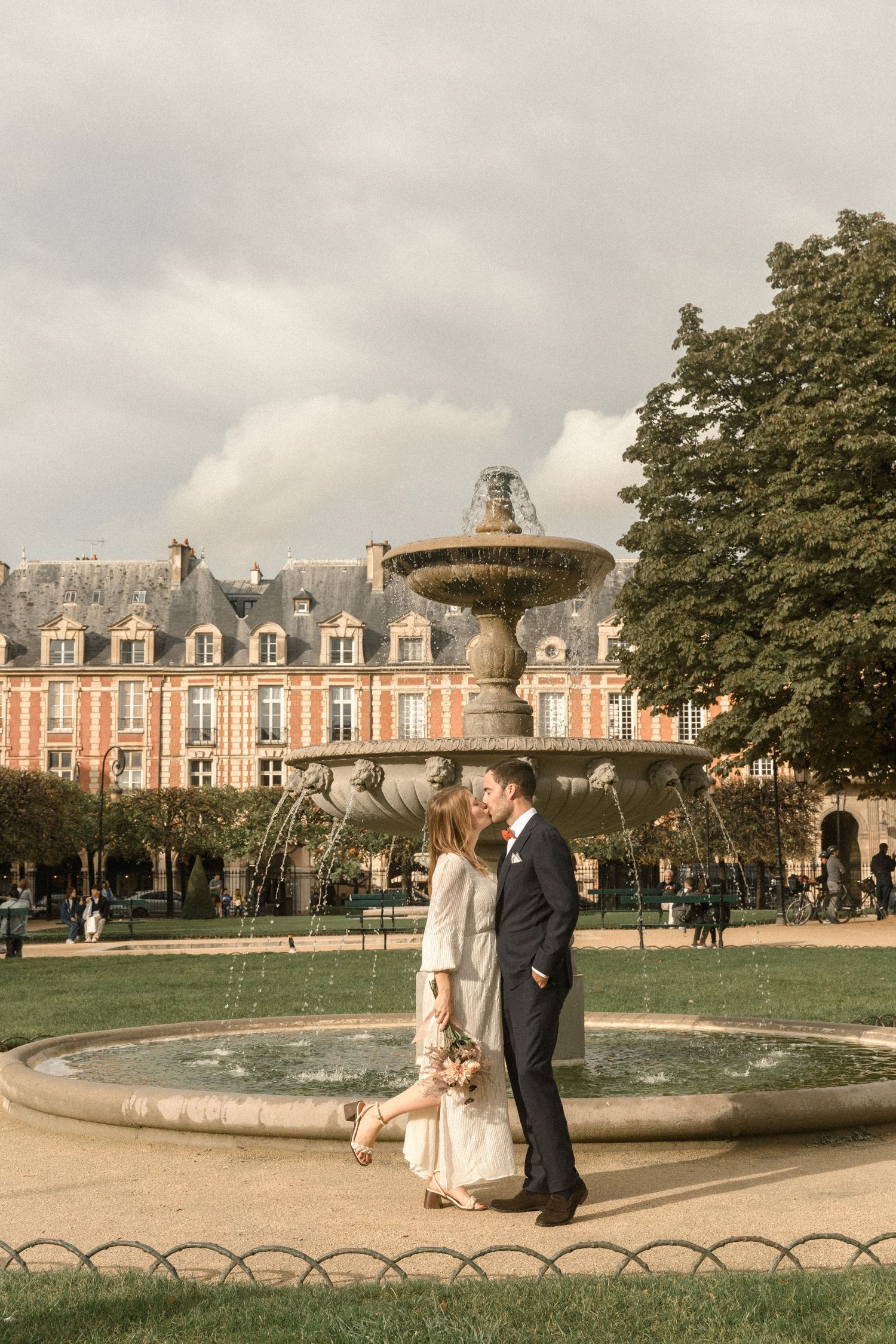 A couple shares an intimate moment by an ornate fountain in a Parisian garden.