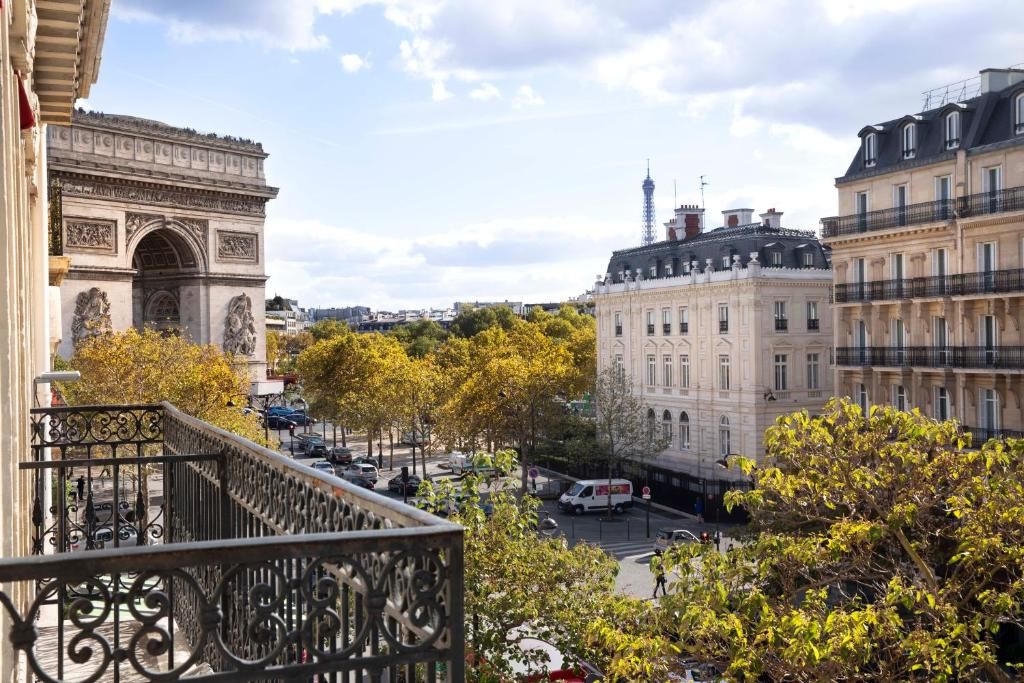 A scenic balcony view of Arc de Triomphe and autumn trees along the Parisian street with classic Haussmann buildings.