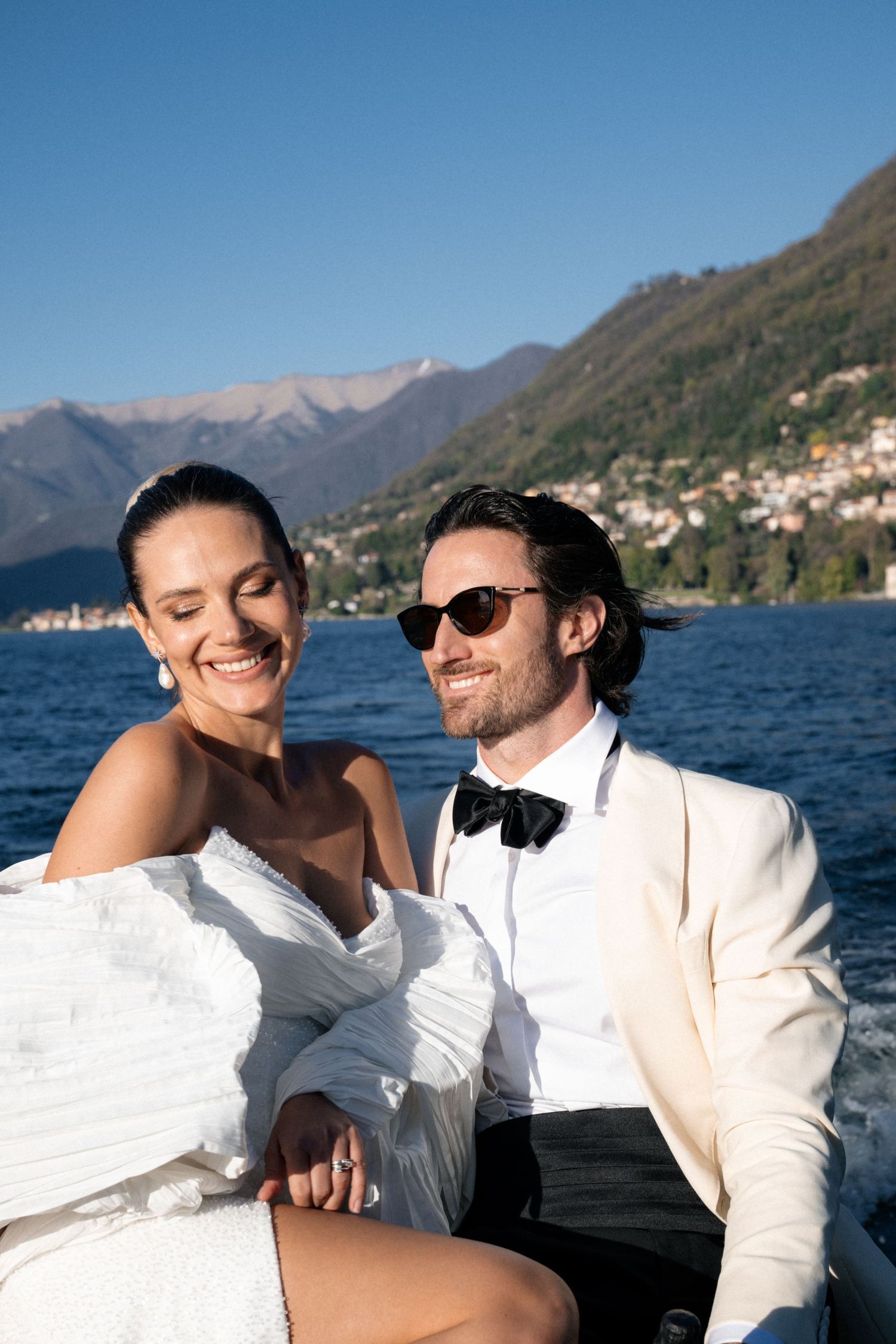 Happy bride and groom sitting together on a boat with stunning Lake Como mountains behind them.