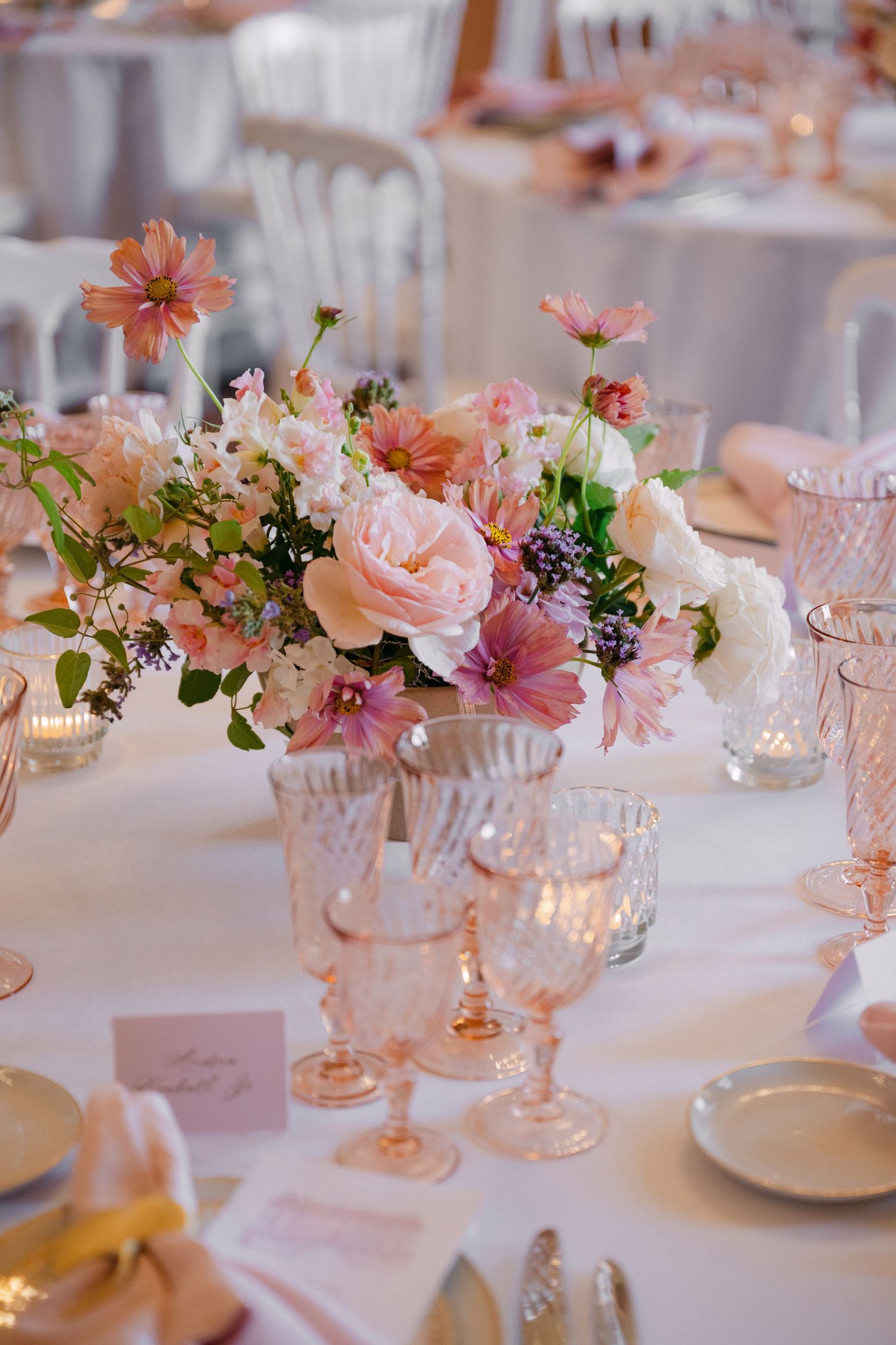 Elegant wedding table setting with pink crystal goblets and a lush floral centerpiece of roses and cosmos blooms.