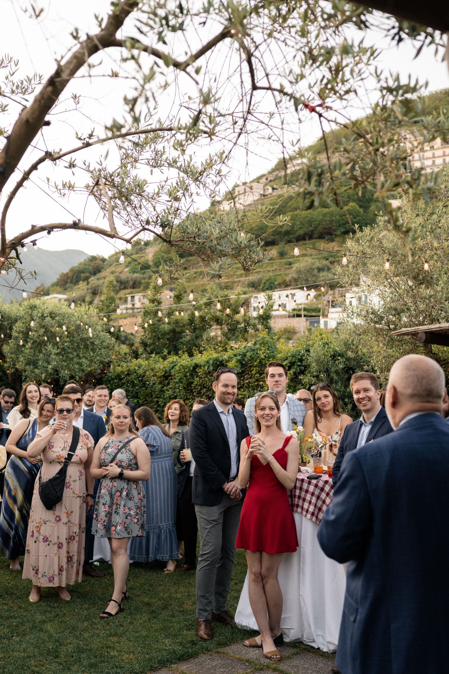 Wedding guests gather outdoors listening to a toast at a scenic Italian hillside reception.