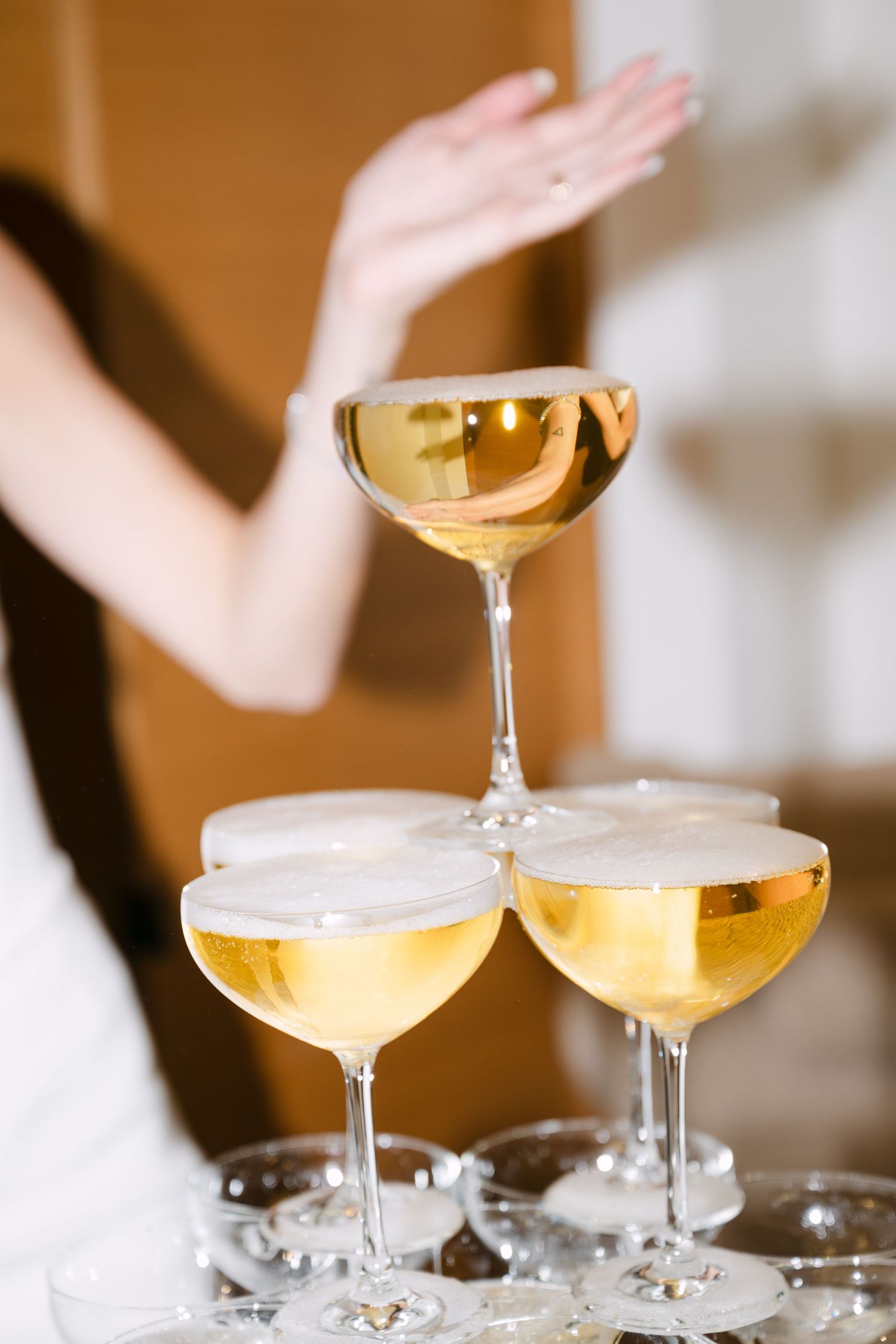 Close-up of a champagne tower with golden bubbly coupe glasses at a wedding celebration.