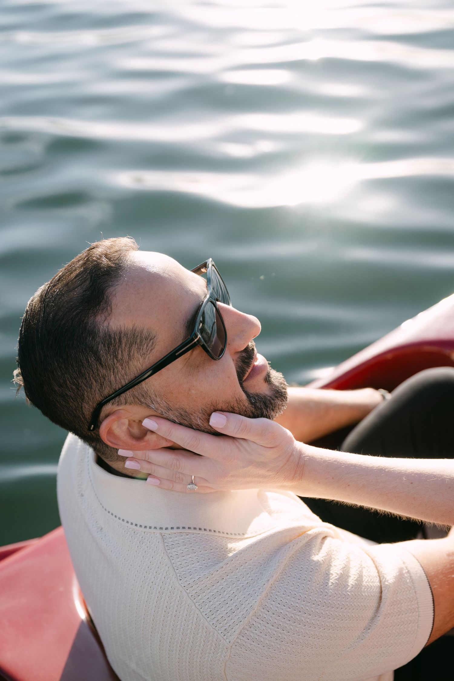 Bearded man in sunglasses relaxing on a red boat with water in the background.